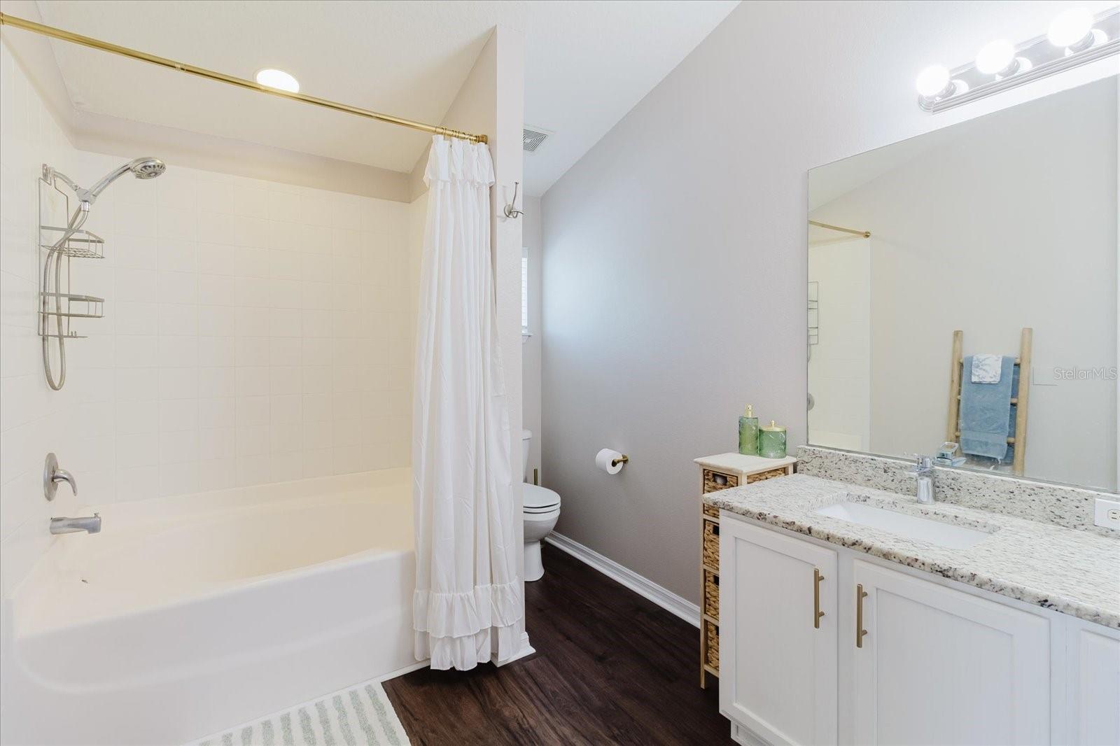 Primary Ensuite Bathroom With Luxury Vinyl Floors, Granite Double Vanity, and Shower With A Generous Soaking Tub