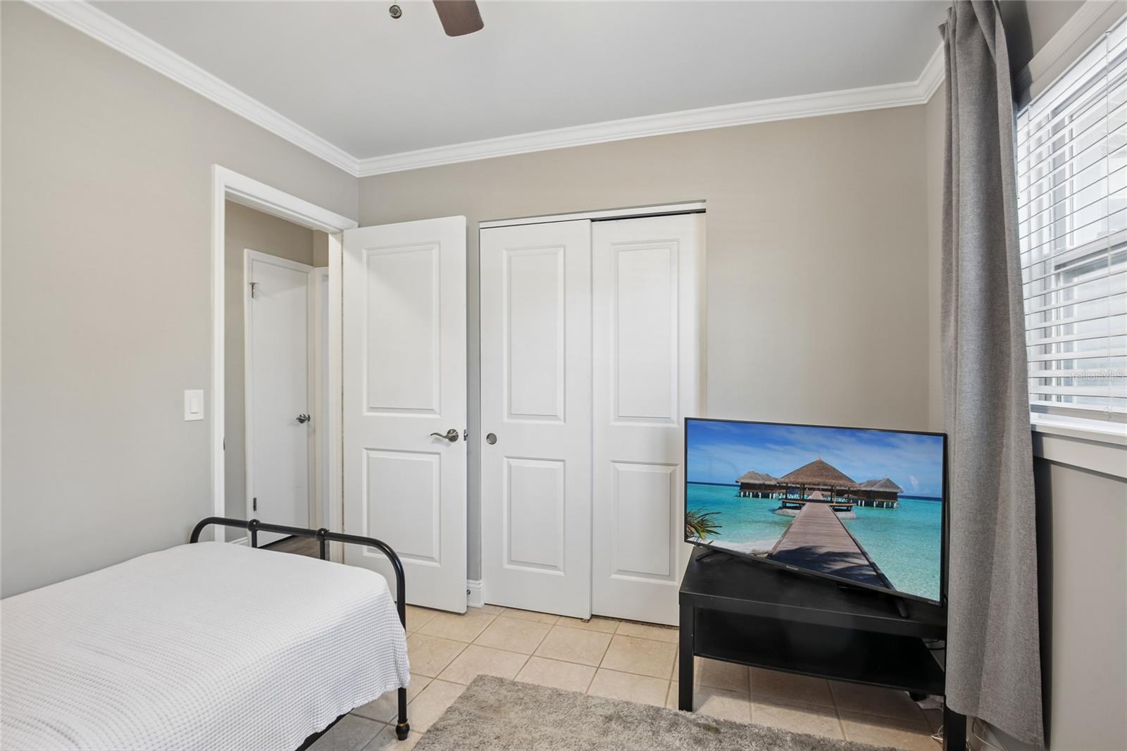 Bedroom Two Closet View – This secondary bedroom includes a double-door closet, neutral wall color, and a mix of tile and carpeted flooring. The window brings in natural light while maintaining a simple, functional layout.