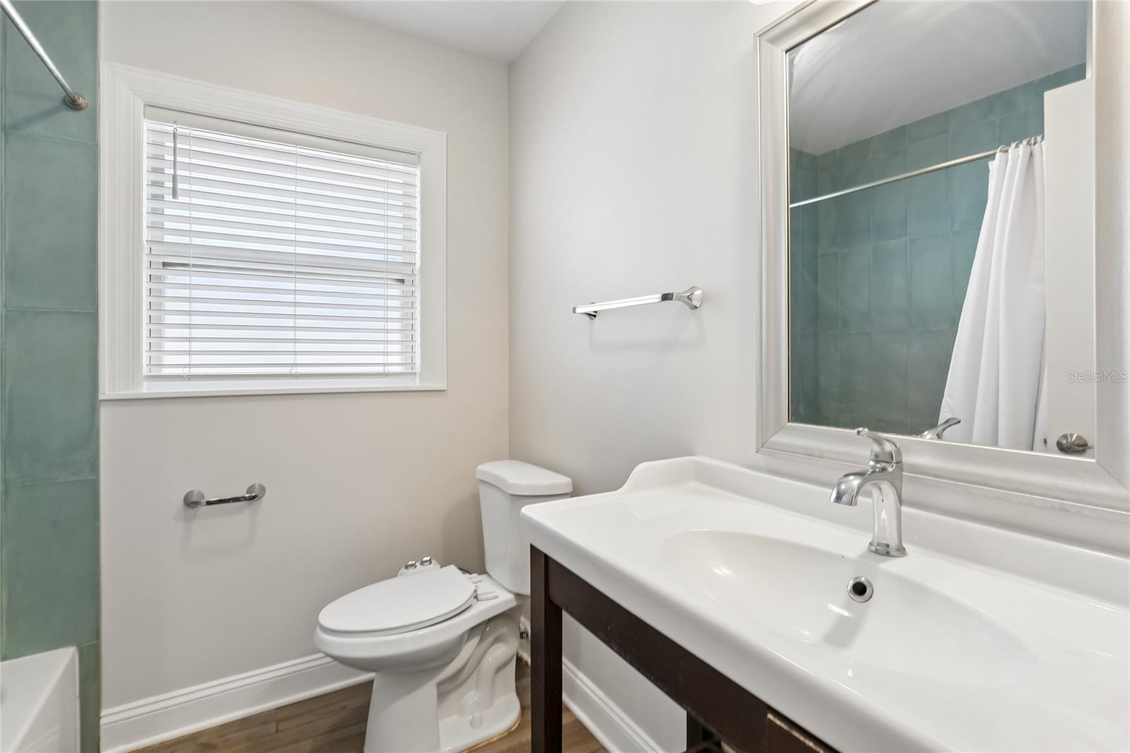 Second Bathroom – The second bathroom features a clean vanity with a framed mirror, chrome fixtures, and a window with blinds for natural light. A tub/shower combination with tile surround adds everyday convenience.