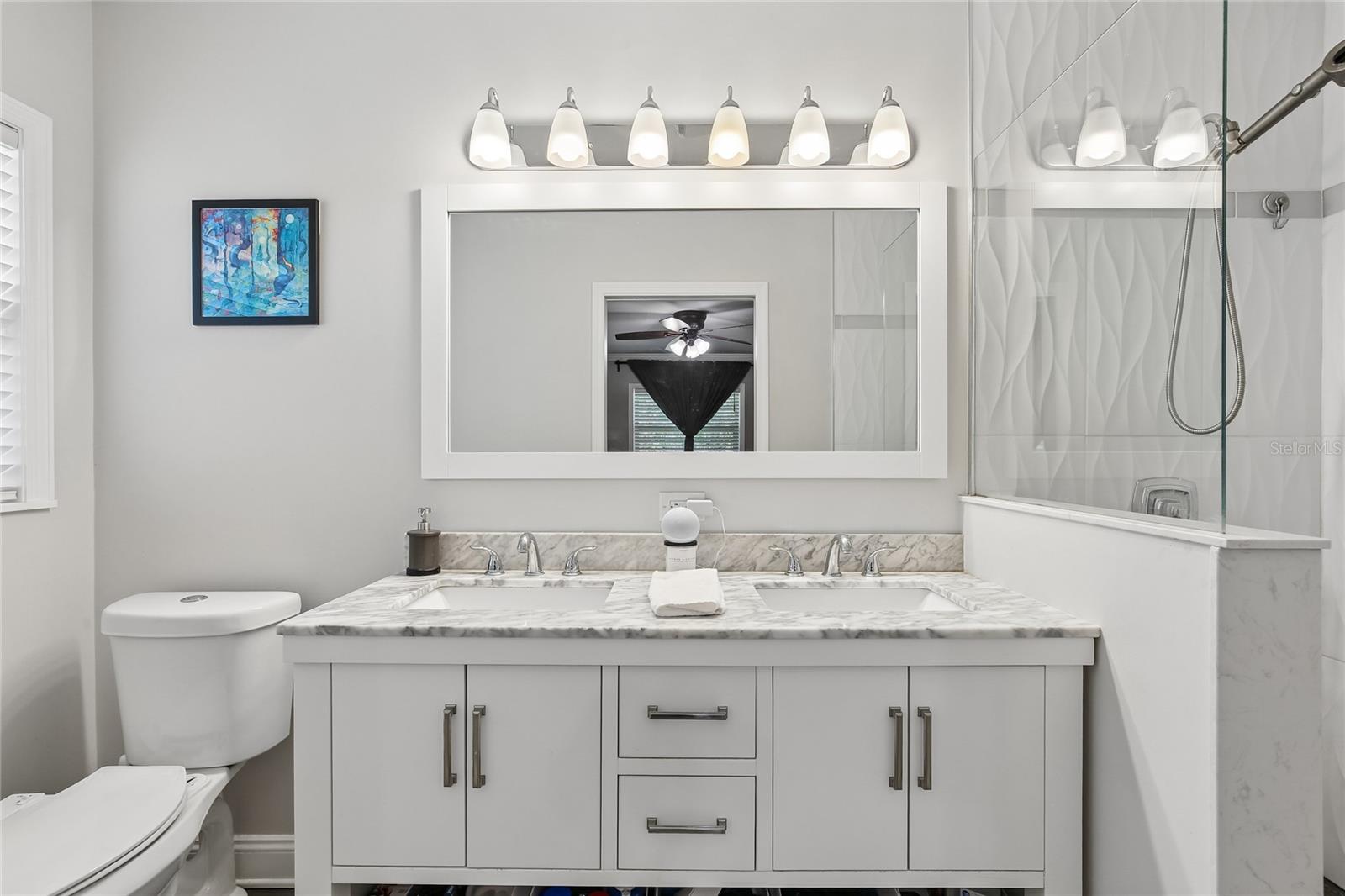 Primary En Suite Bathroom – The primary en suite bathroom features a dual-sink vanity with a marble-look countertop, updated cabinetry, and a wide framed mirror with bright vanity lighting. Clean finishes and a neutral palette give the space a fresh, polished feel.