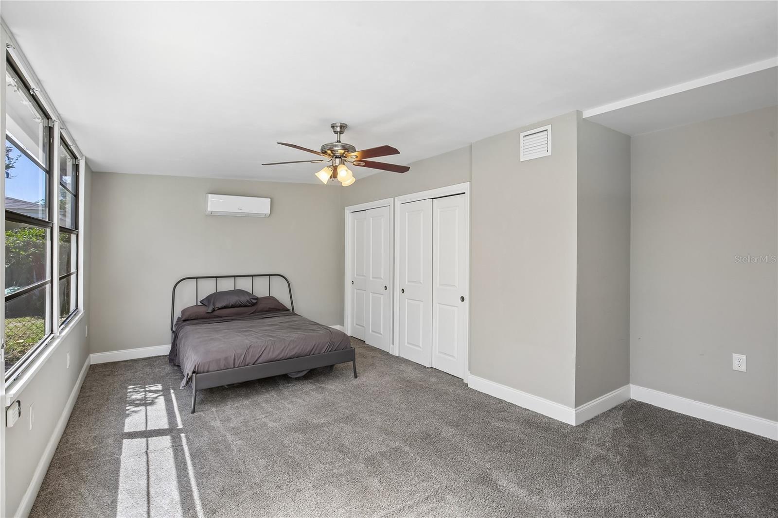 Fourth Bedroom - The fourth bedroom offers a spacious layout with plush carpeting, a ceiling fan, double-door closet, and a wall-mounted mini-split system. Located just off the bonus room by the pool, it provides flexible use as a guest room, private retreat, or additional living space.