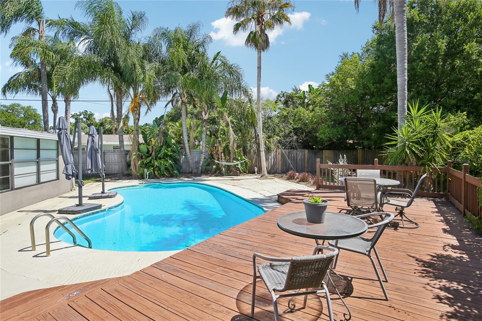 Poolside Entertaining Area – The wood deck overlooks the pool and offers a comfortable setting for outdoor dining or lounging. Lush greenery and privacy fencing create a peaceful backyard backdrop.