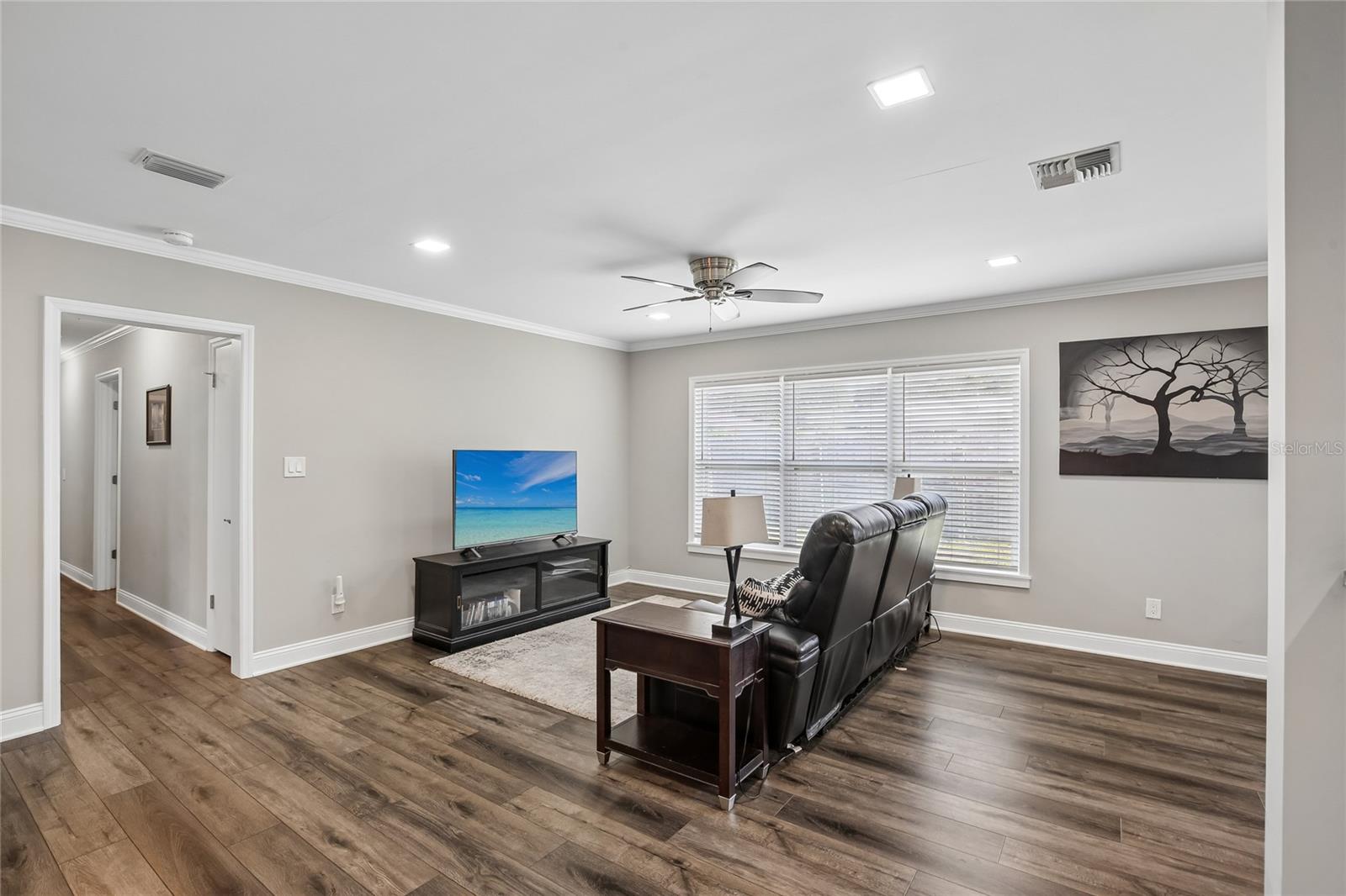 Living Room – The spacious living room offers clean lines, crown molding, recessed lighting, and a large front window with blinds. The open layout provides flexibility for everyday living and entertaining.