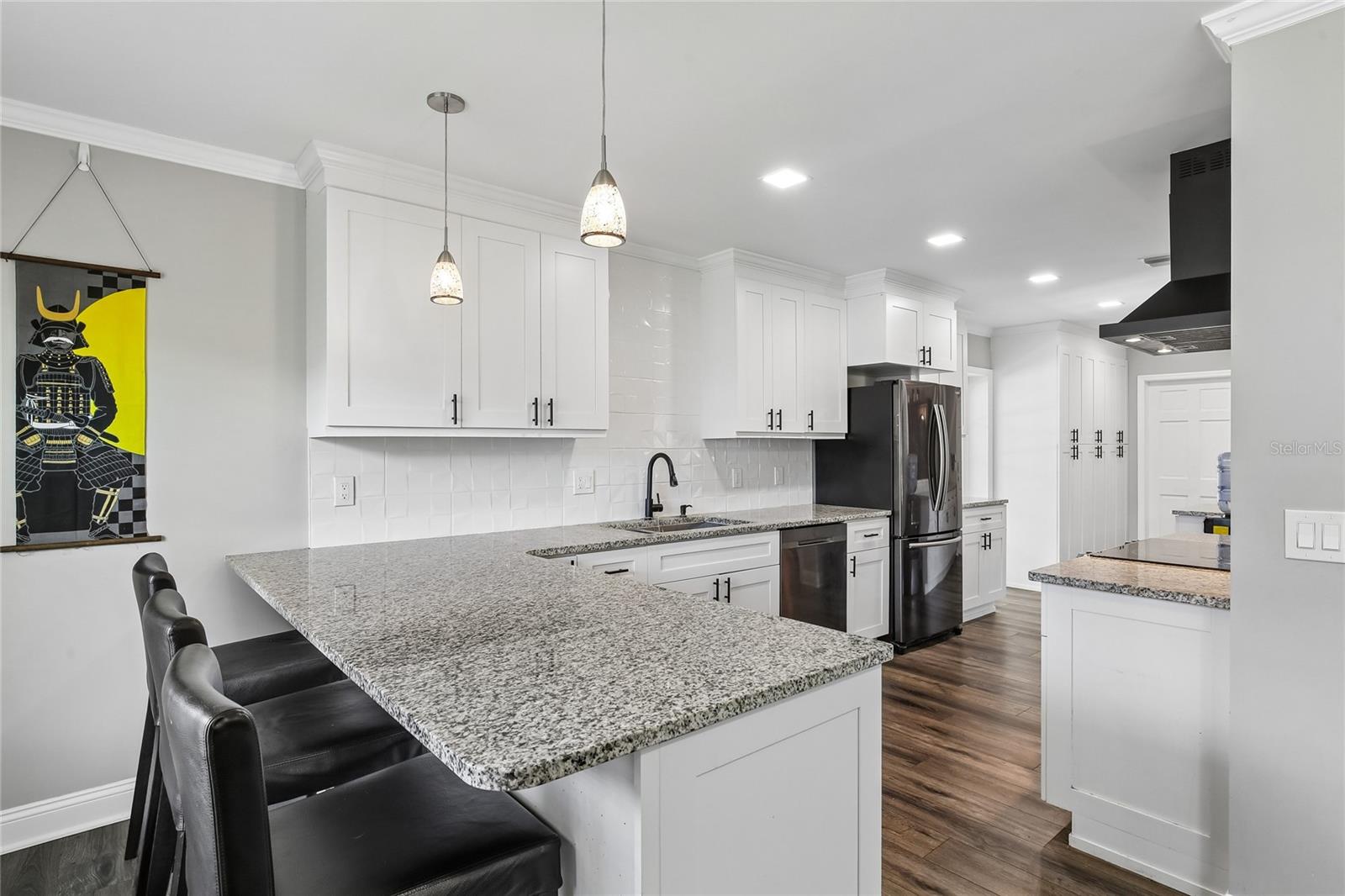 Kitchen Breakfast Bar – The kitchen features a spacious granite breakfast bar with pendant lighting and seating space, creating an inviting spot for casual dining. White cabinetry, a tile backsplash, and dark hardware add a clean, updated look.