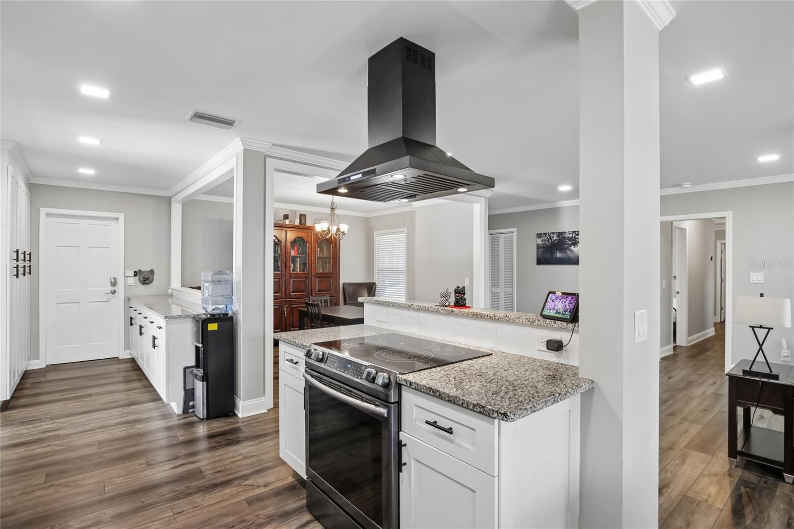 Kitchen Cooktop Area – The kitchen includes a sleek range with a statement hood, granite countertops, and white cabinetry with dark hardware. The open sightlines connect the cooking area to the dining and living spaces.