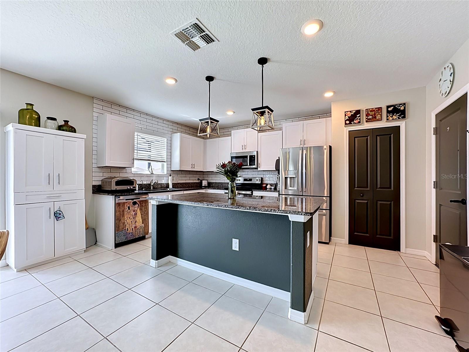 Well-appointed kitchen with granite countertops, spacious island with breakfast bar seating, stainless steel appliances, subway tile backsplash, abundant cabinetry, and updated pendant lighting