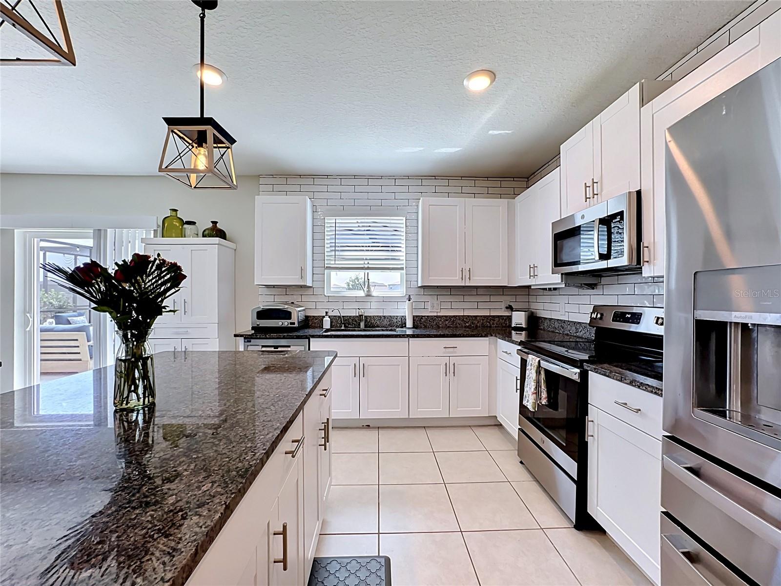 Well-appointed kitchen with granite countertops, spacious island with breakfast bar seating, stainless steel appliances, subway tile backsplash, abundant cabinetry, and updated pendant lighting