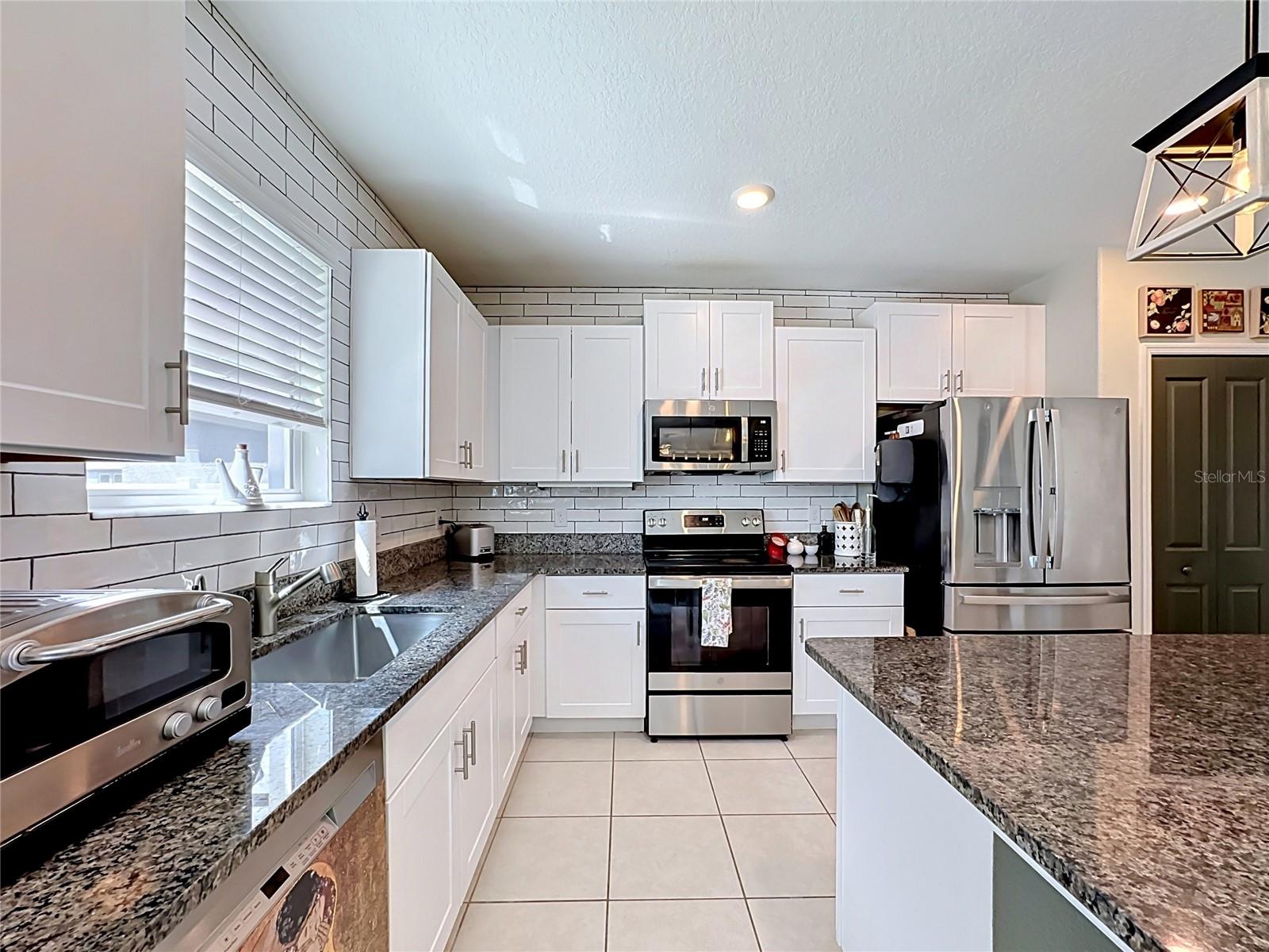 Well-appointed kitchen with granite countertops, spacious island with breakfast bar seating, stainless steel appliances, subway tile backsplash, abundant cabinetry, and updated pendant lighting