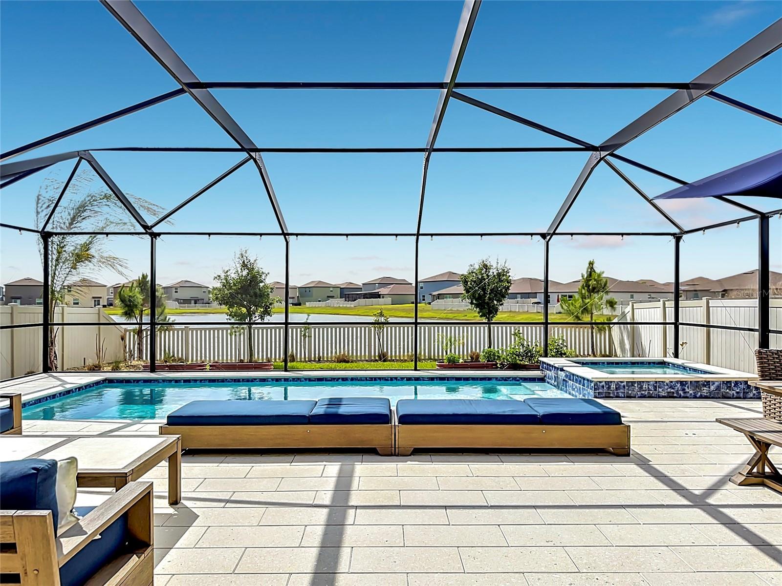 Backyard oasis featuring an enclosed heated saltwater pool and spa, expansive paver decking, and tranquil pond views
