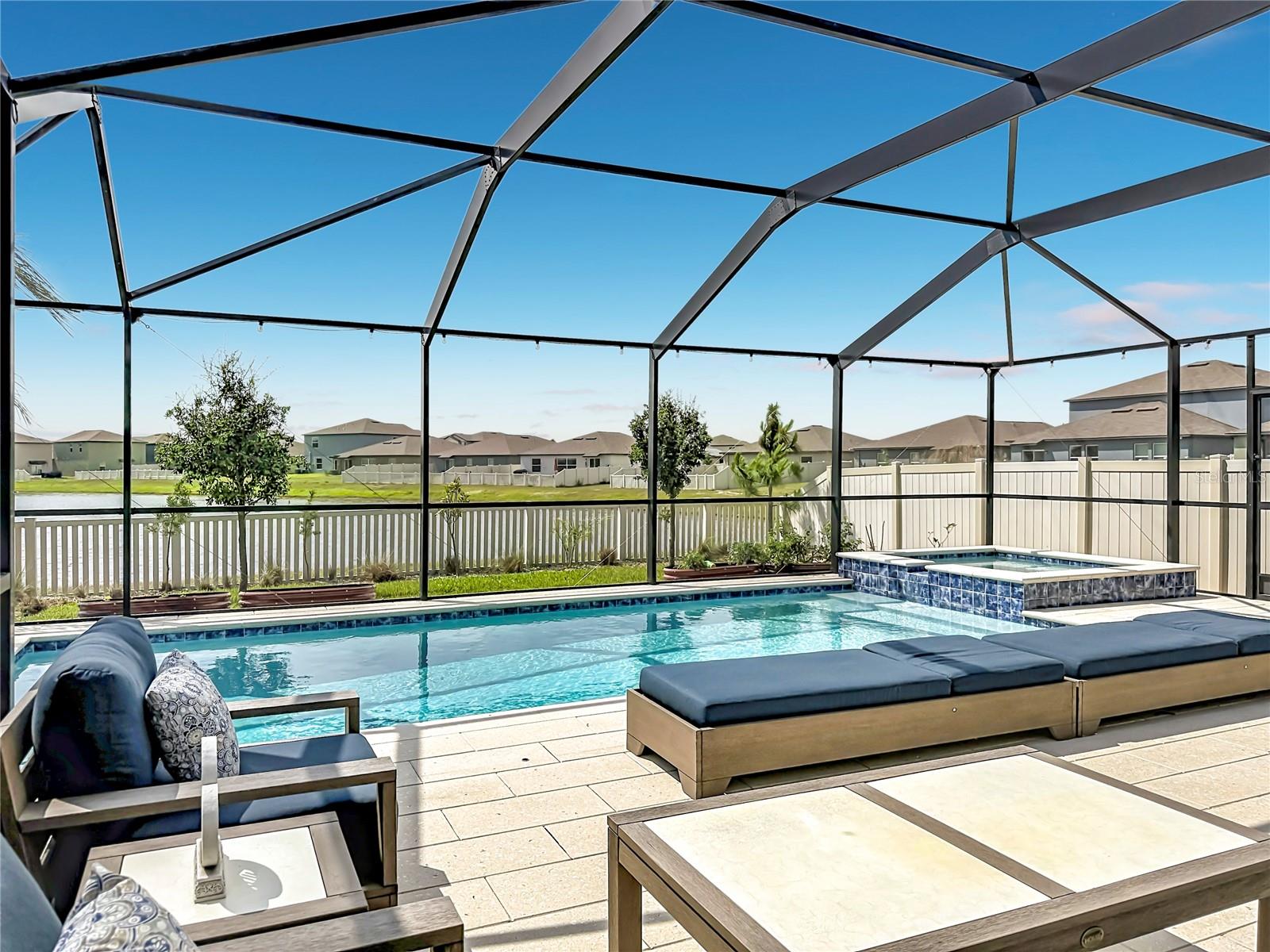Backyard oasis featuring an enclosed heated saltwater pool and spa, expansive paver decking, and tranquil pond views