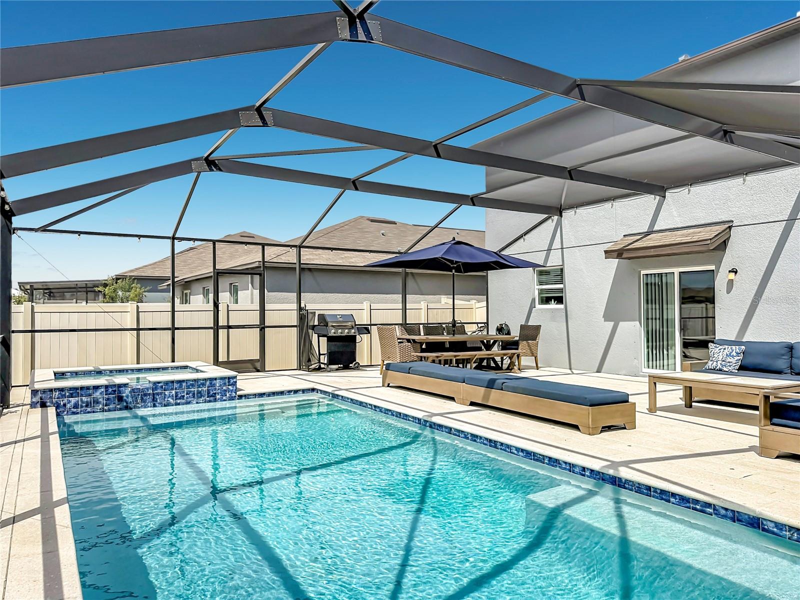Backyard oasis featuring an enclosed heated saltwater pool and spa, expansive paver decking, and tranquil pond views
