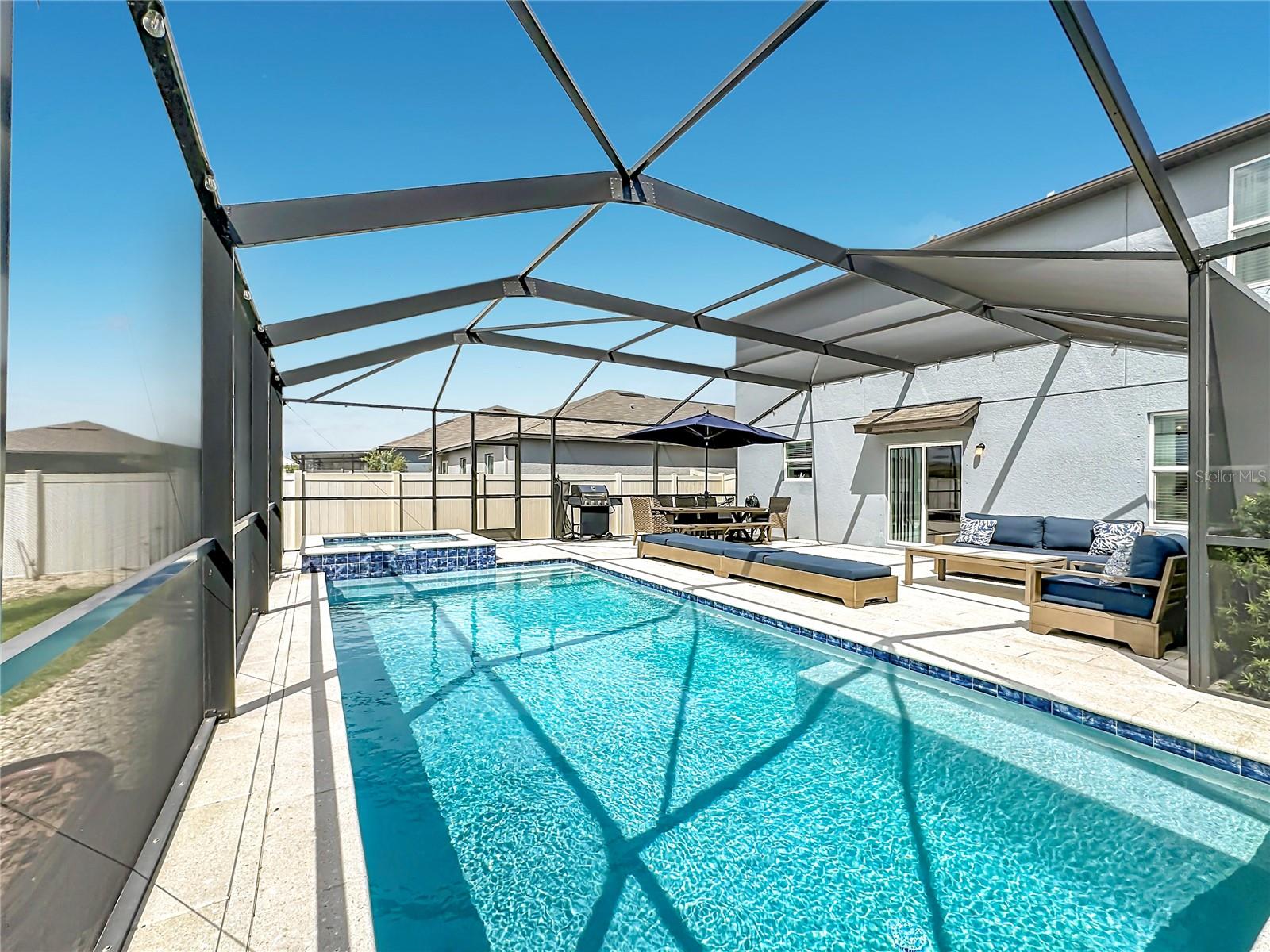 Backyard oasis featuring an enclosed heated saltwater pool and spa, expansive paver decking, and tranquil pond views