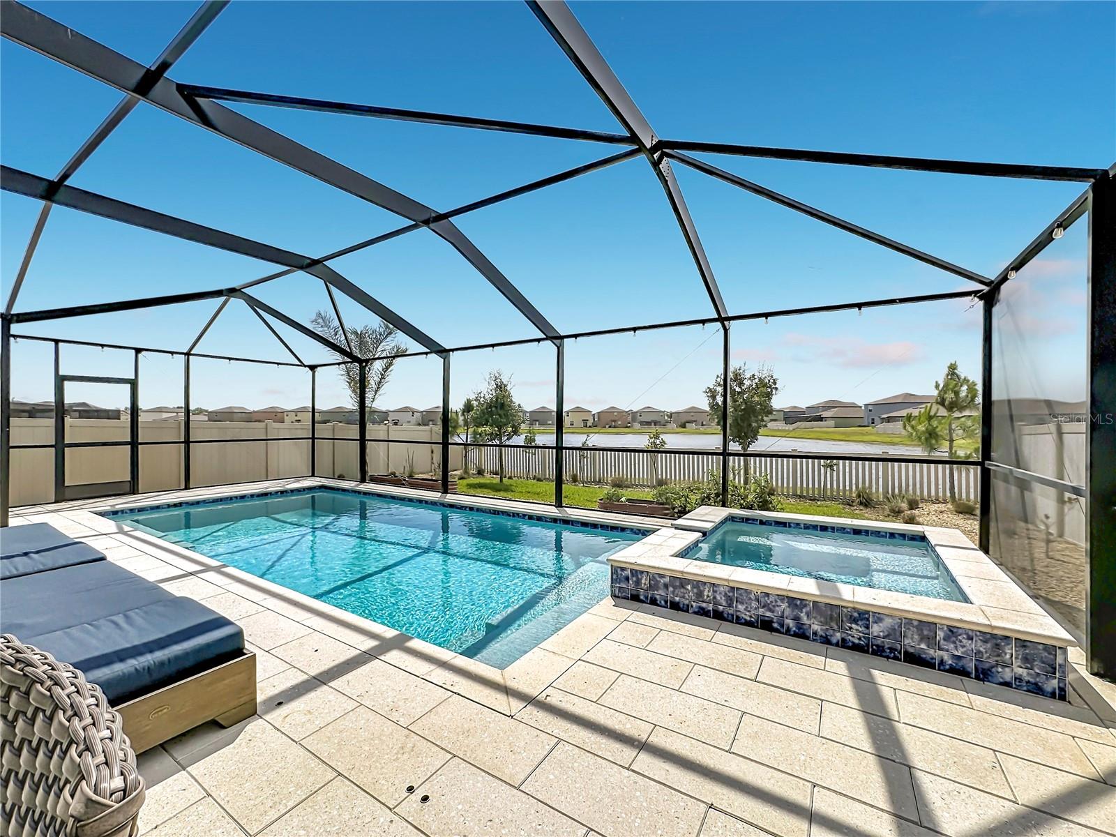 Backyard oasis featuring an enclosed heated saltwater pool and spa, expansive paver decking, and tranquil pond views
