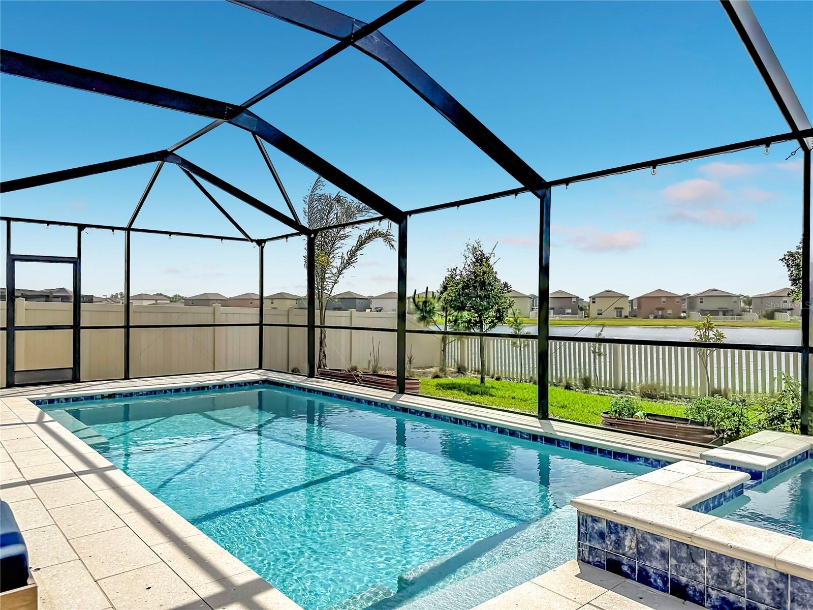 Backyard oasis featuring an enclosed heated saltwater pool and spa, expansive paver decking, and tranquil pond views