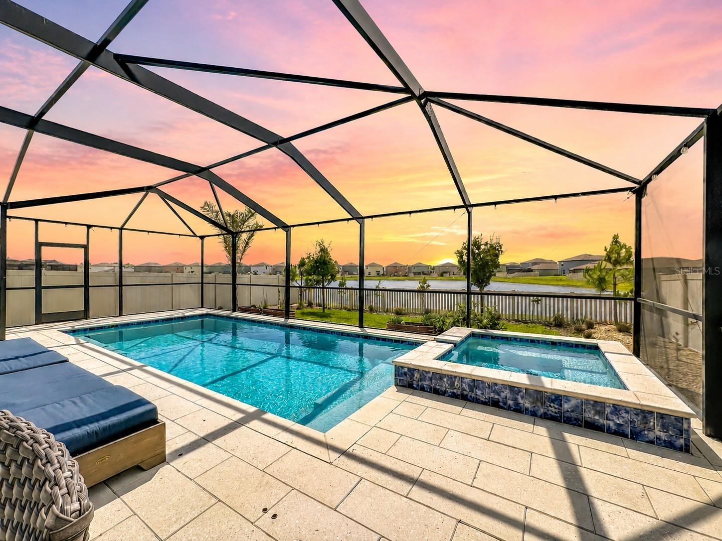Backyard oasis featuring an enclosed heated saltwater pool and spa, expansive paver decking, and tranquil pond views