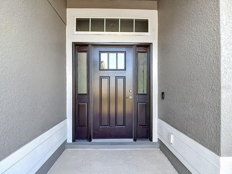 A stately front entrance featuring a rich, dark color accented by decorative glass panels and transom window that fills the space with natural light