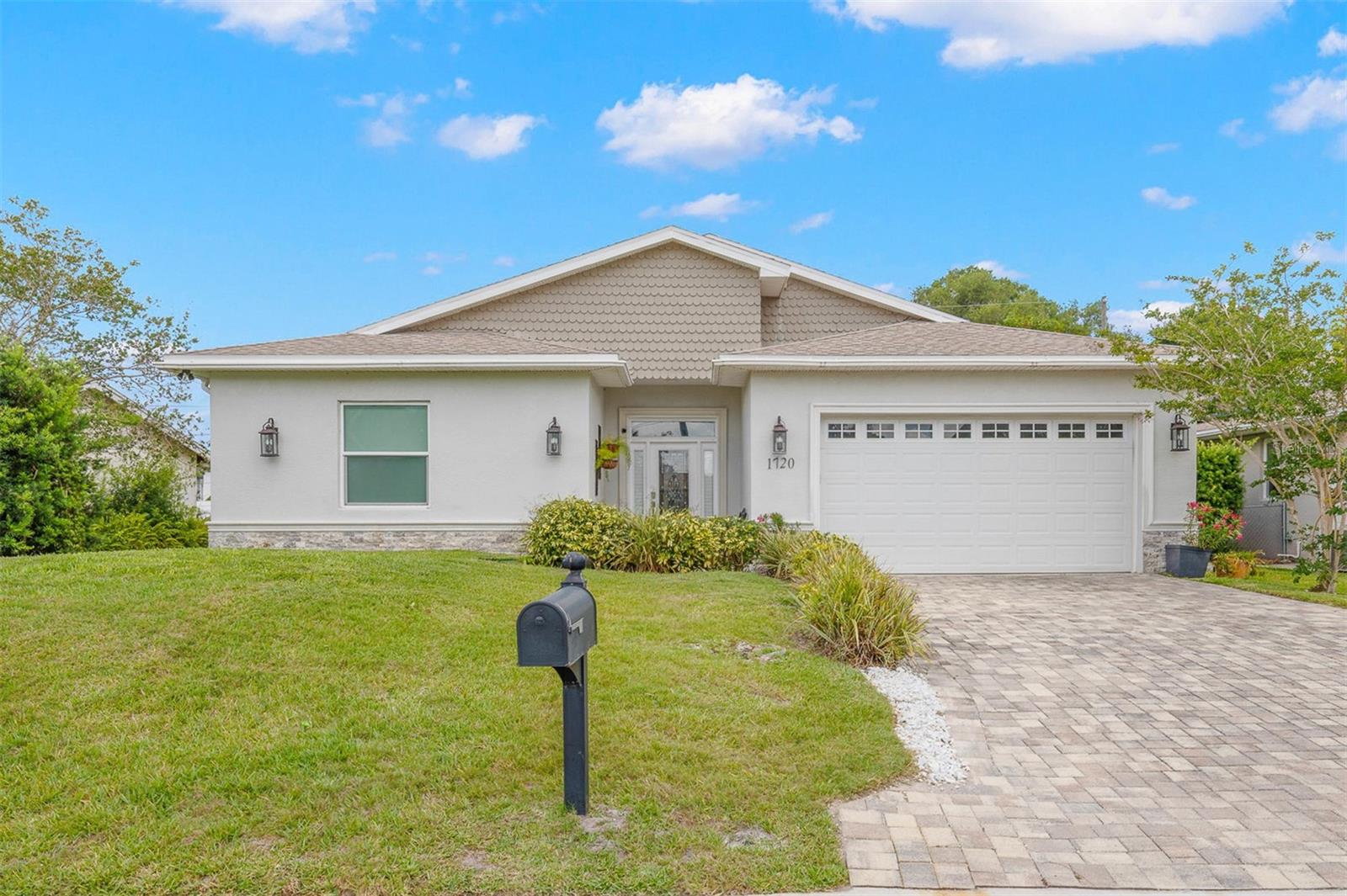 Contemporary coastal styling meets quality construction in this beautifully finished residence featuring a brick paver driveway, oversized 2-car garage, manicured landscaping, decorative exterior lighting, and a welcoming covered entry with leaded glass front door and sidelights.