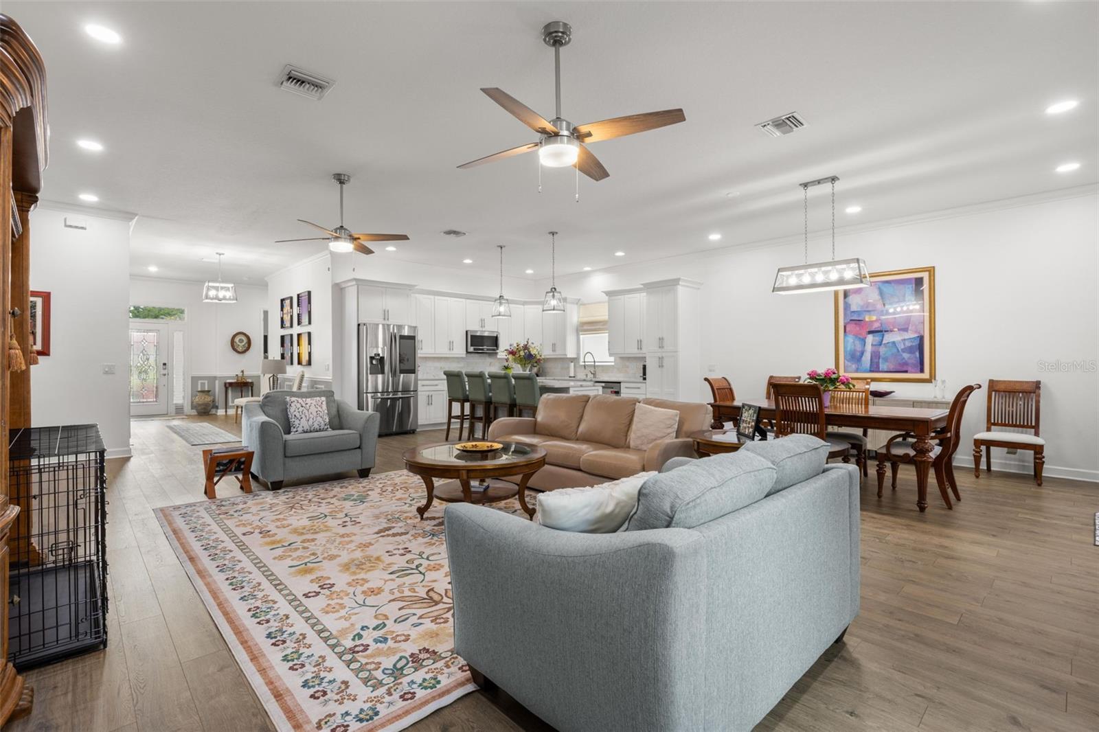 The open great room layout offers generous living and dining spaces beneath high ceilings with crown molding, recessed lighting, and dual contemporary ceiling fans. Wide-plank luxury vinyl flooring carries throughout the main living areas, while the oversized kitchen island creates a natural centerpiece for gathering and conversation.