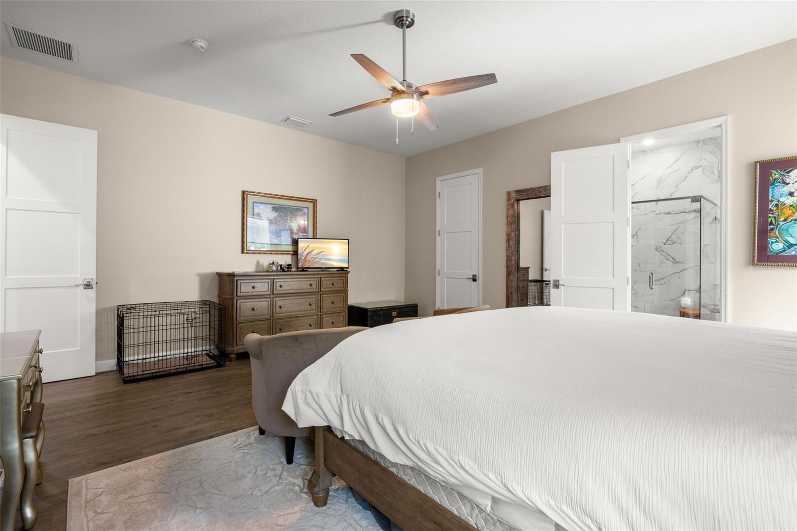 The generously sized primary suite offers a spacious layout with wide-plank luxury vinyl flooring, neutral finishes, oversized paneled doors, and a contemporary ceiling fan. The private ensuite bath features designer tile finishes, while the oversized walk-in closet provides substantial storage space.