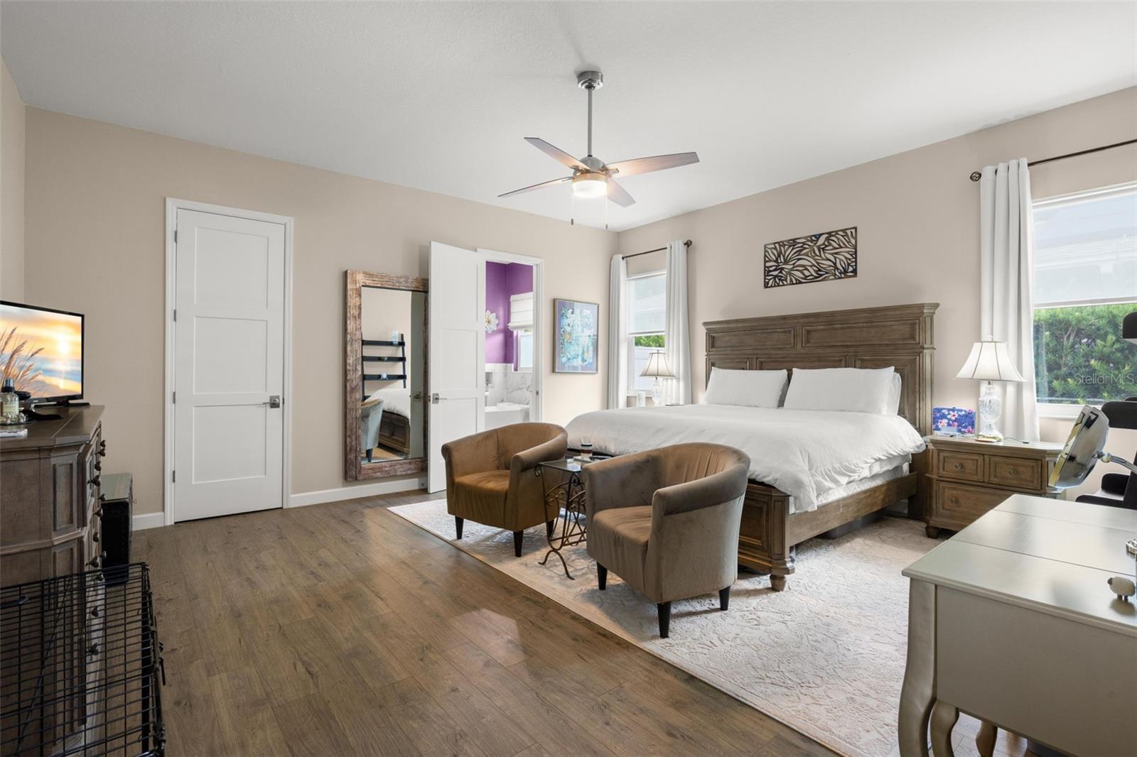 The oversized primary bedroom features wide-plank luxury vinyl flooring, neutral finishes, oversized paneled doors, and a contemporary ceiling fan. With room for a sitting area and direct access to the ensuite bath and walk-in closet, the spacious layout offers both comfort and functionality.