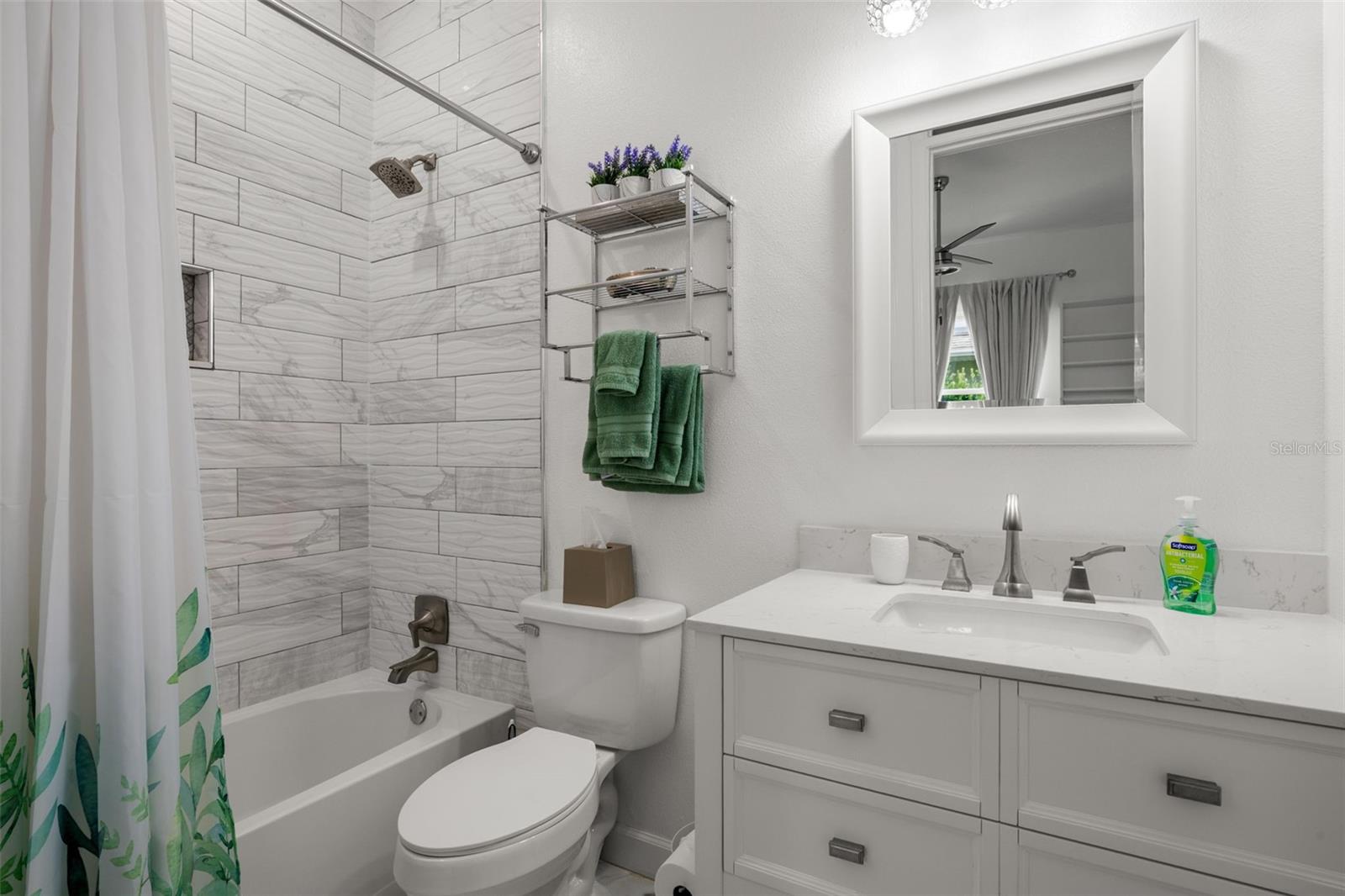 Bedroom 3 ensuite bath features a tub with shower, marble-look tile extending to the ceiling, a mirrored vanity with quartz countertop, upgraded fixtures, and a built-in shower niche.
