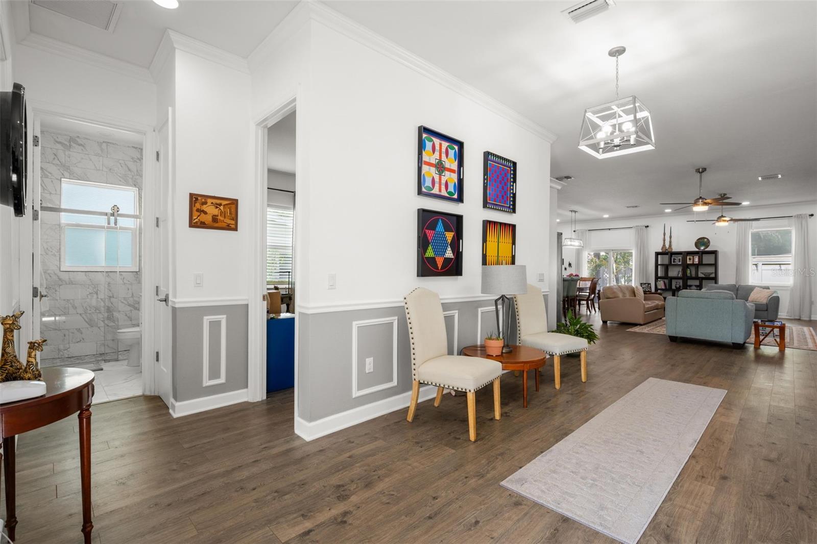The oversized foyer offers an elegant introduction to the home with extensive crown molding, oversized base trim, wainscoting, chair rail detailing, recessed lighting, a statement chandelier, and wide-plank luxury vinyl flooring. Open sightlines lead directly into the expansive main living areas, while the split-bedroom layout provides privacy and flexibility.