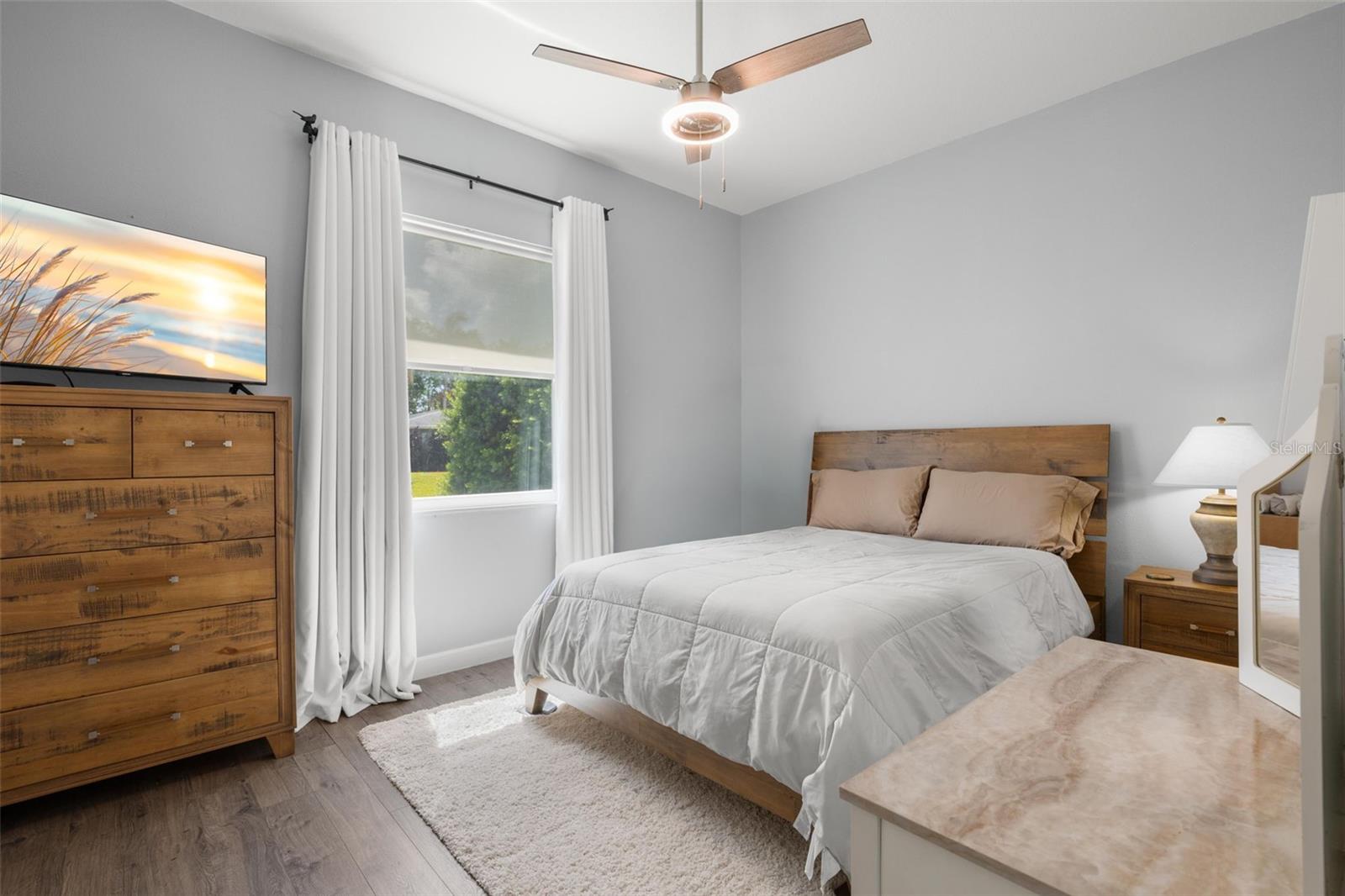 Bedroom 2 features wide-plank luxury vinyl flooring, a contemporary ceiling fan, abundant natural light, and a soft neutral color palette.