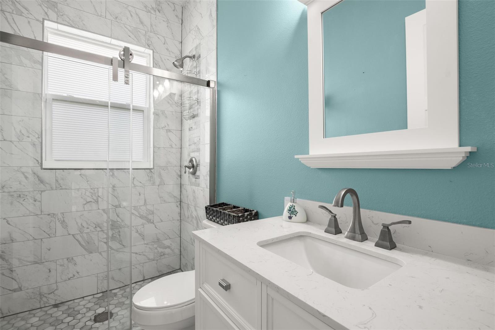 Bathroom 2 features a frameless glass walk-in shower with marble-look tile, quartz countertop vanity, upgraded fixtures, and abundant natural light.