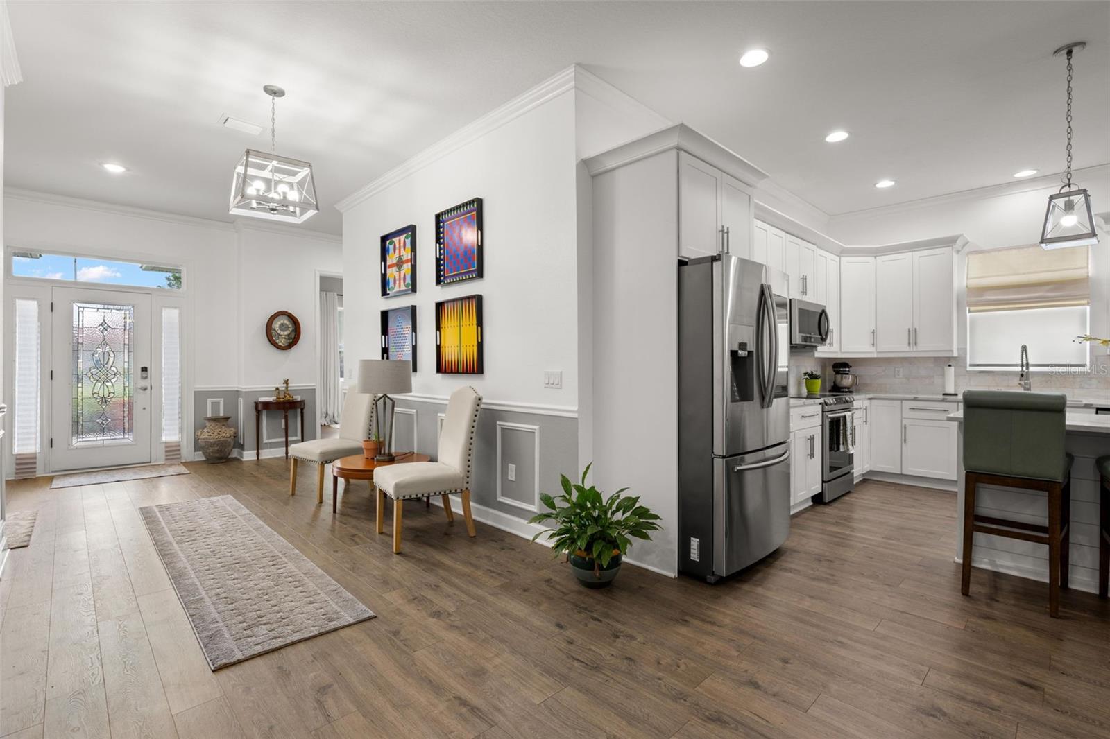 The oversized foyer makes an immediate impression with wide-plank luxury vinyl flooring, extensive crown molding, wainscoting, chair rail detailing, recessed lighting, and an elegant leaded glass entry door with sidelights.