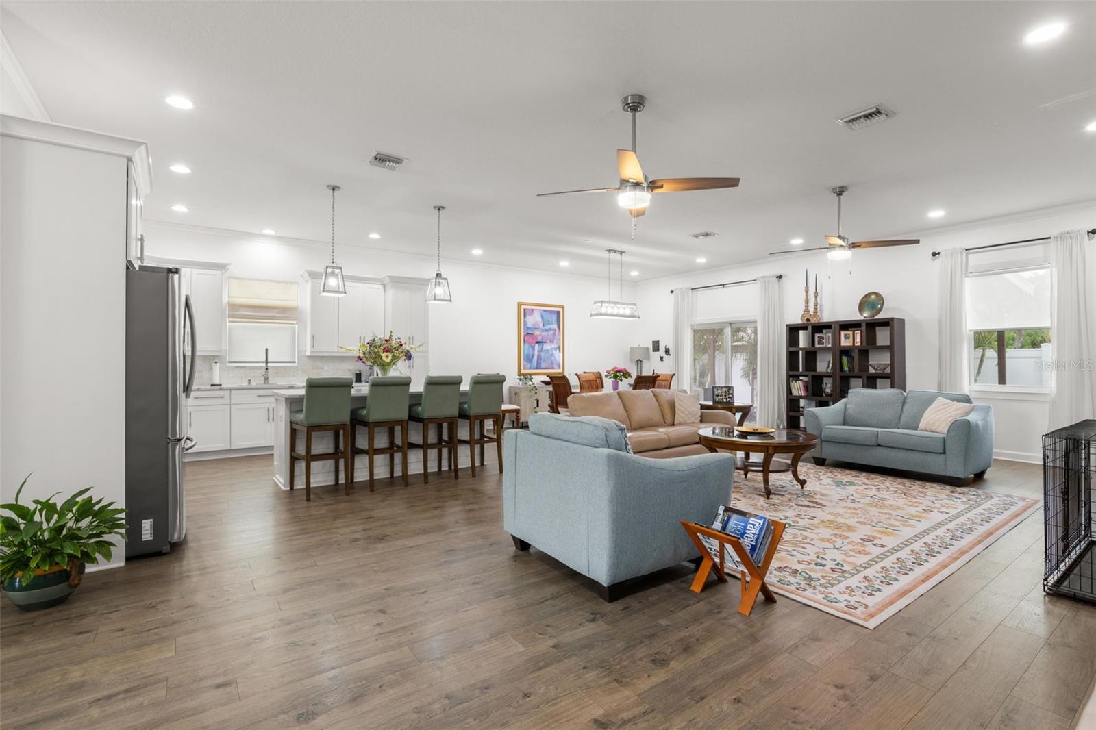 The expansive open-concept layout features wide-plank luxury vinyl flooring, recessed lighting, crown molding, and seamless flow between the great room, dining area, and chef-inspired kitchen. High ceilings and abundant natural light enhance the airy feel, while oversized impact windows and sliding glass doors bring the outdoors in.