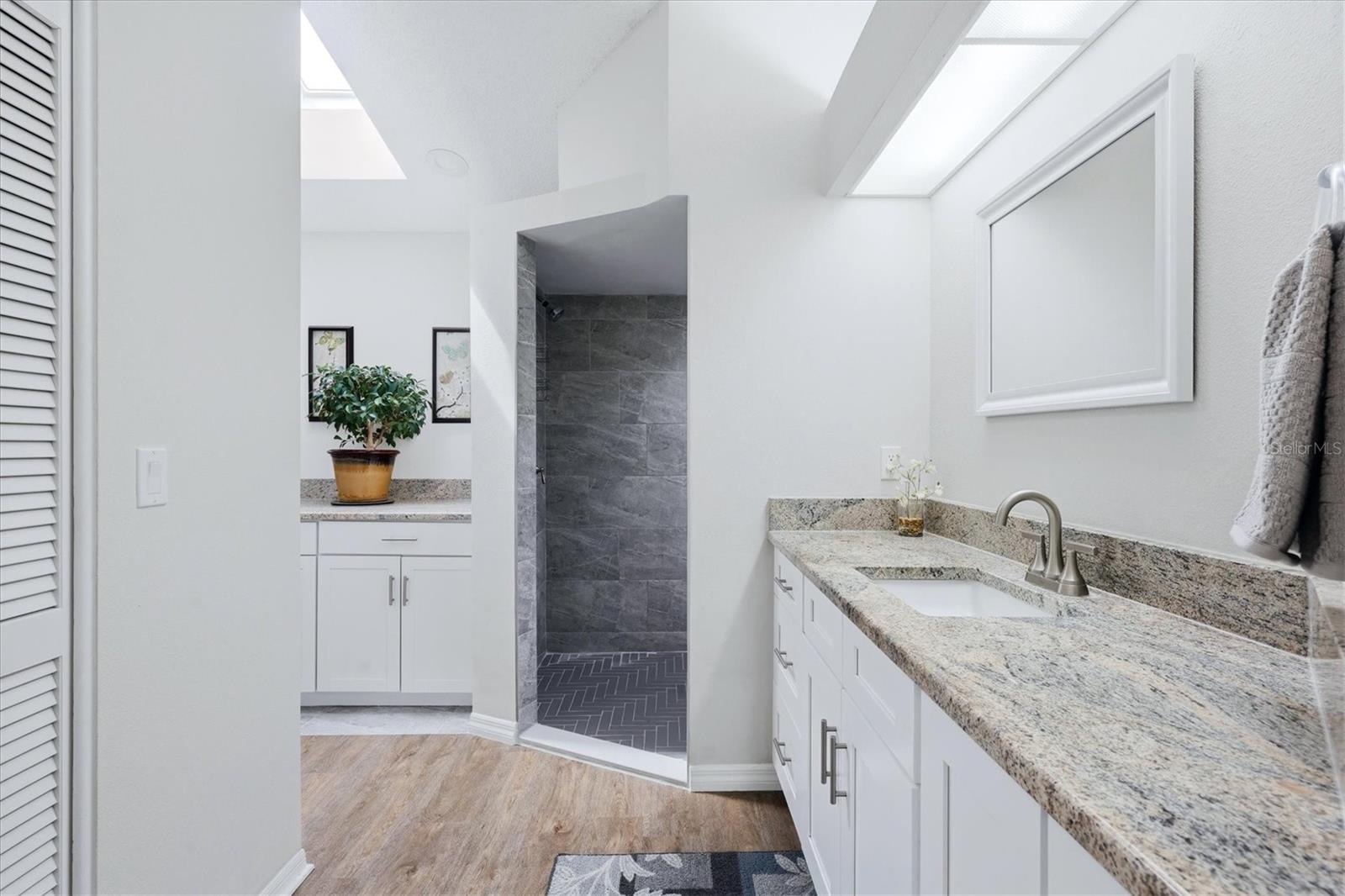 PRIMARY EN-SUITE BATHROOM WITH SKYLIGHT, DUAL CLOSETS WALKIN AND BUILT IN, TALL VANITEIS AND GRANITE COUNTER TOP, WLAK IN SHOWER WITH HERRINGBONE TILE SHOWER FLOOR AND NICHE