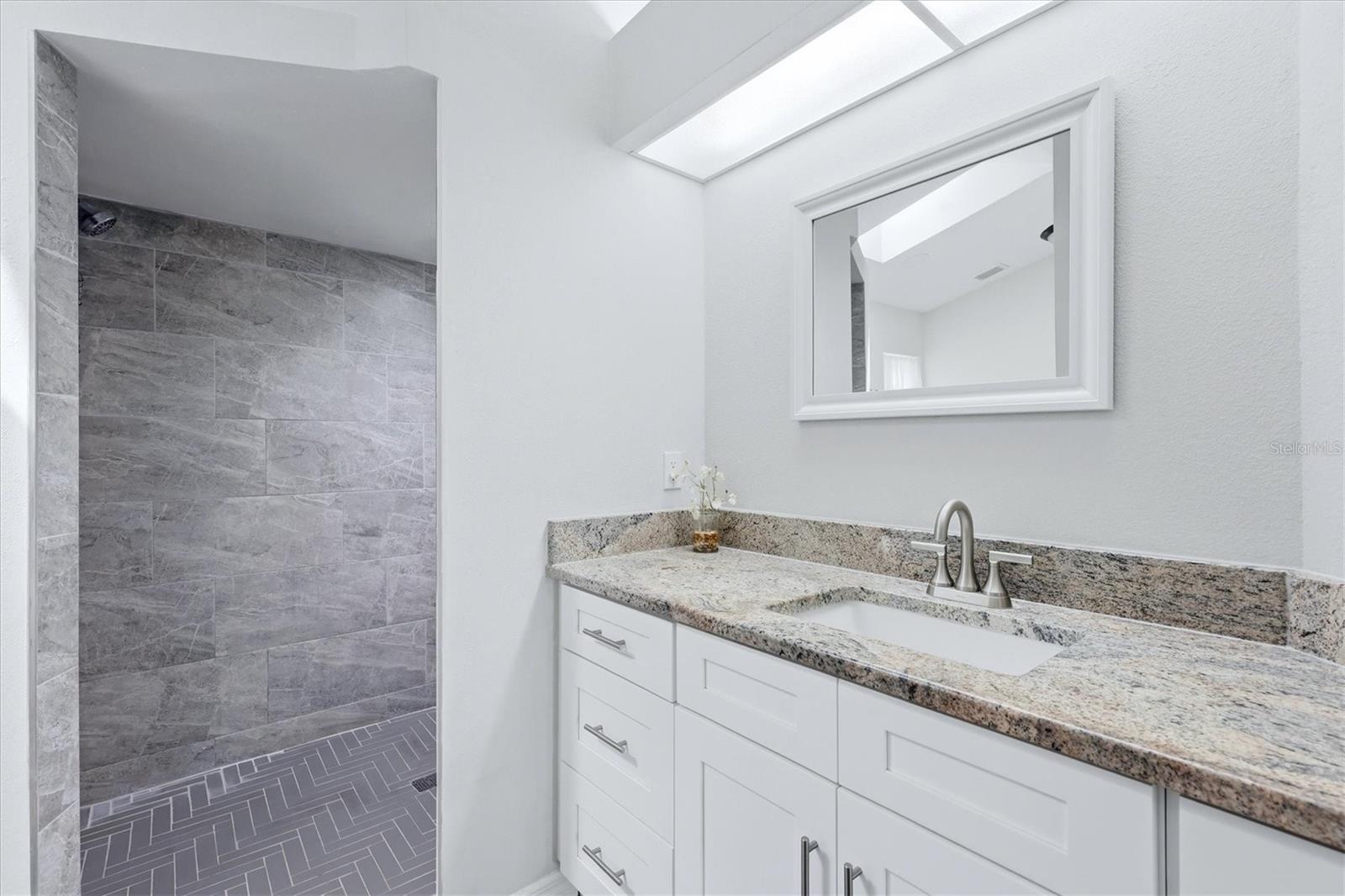 PRIMARY EN-SUITE BATHROOM WITH SKYLIGHT, DUAL CLOSETS WALKIN AND BUILT IN, TALL VANITEIS AND GRANITE COUNTER TOP, WLAK IN SHOWER WITH HERRINGBONE TILE SHOWER FLOOR AND NICHE
