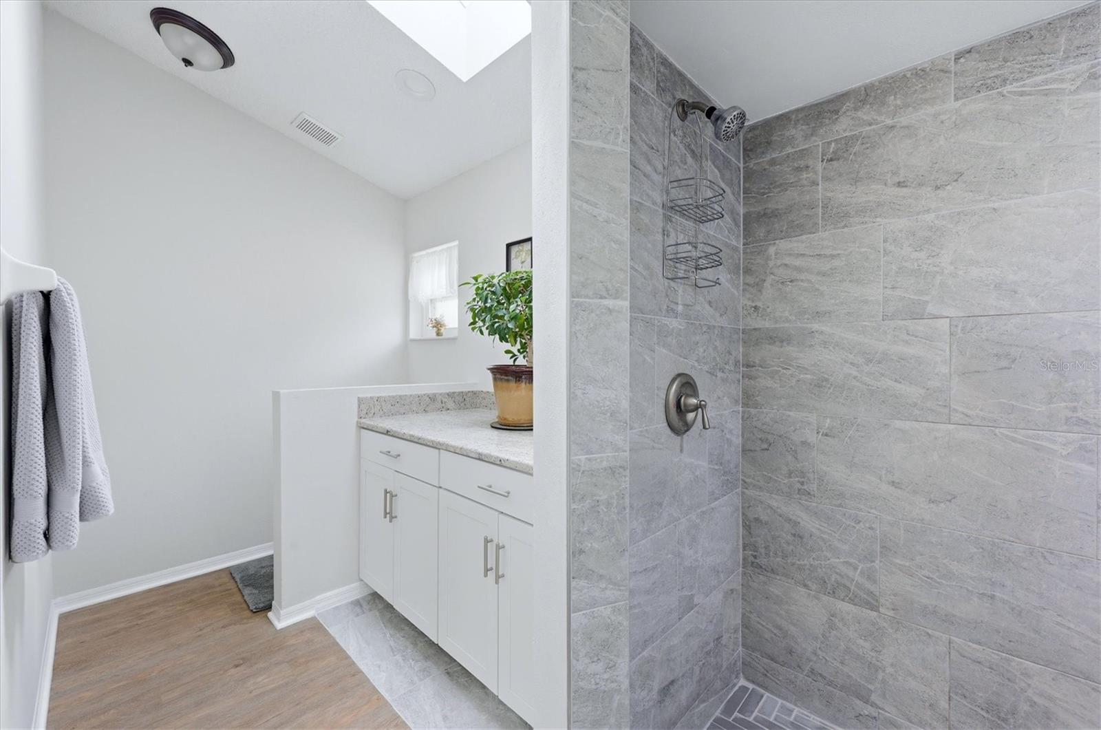 PRIMARY EN-SUITE BATHROOM WITH SKYLIGHT, DUAL CLOSETS WALKIN AND BUILT IN, TALL VANITEIS AND GRANITE COUNTER TOP, WLAK IN SHOWER WITH HERRINGBONE TILE SHOWER FLOOR AND NICHE