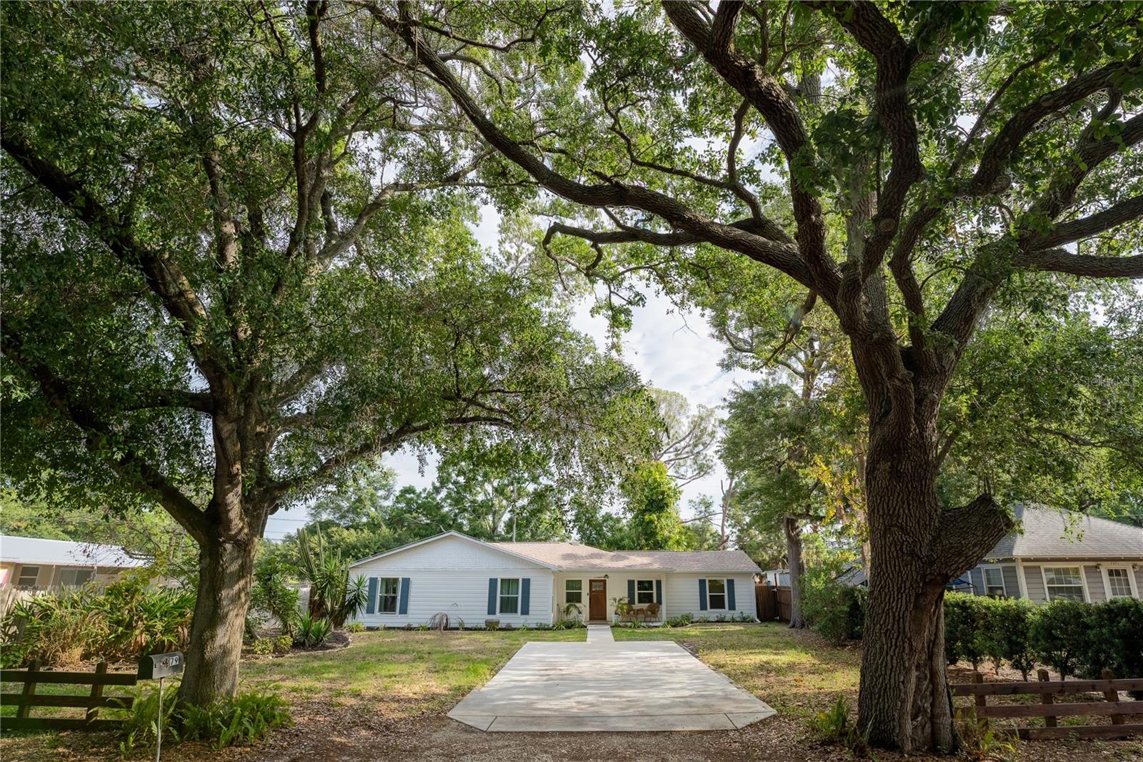 Front of home with large yard and trees at the end of driveway