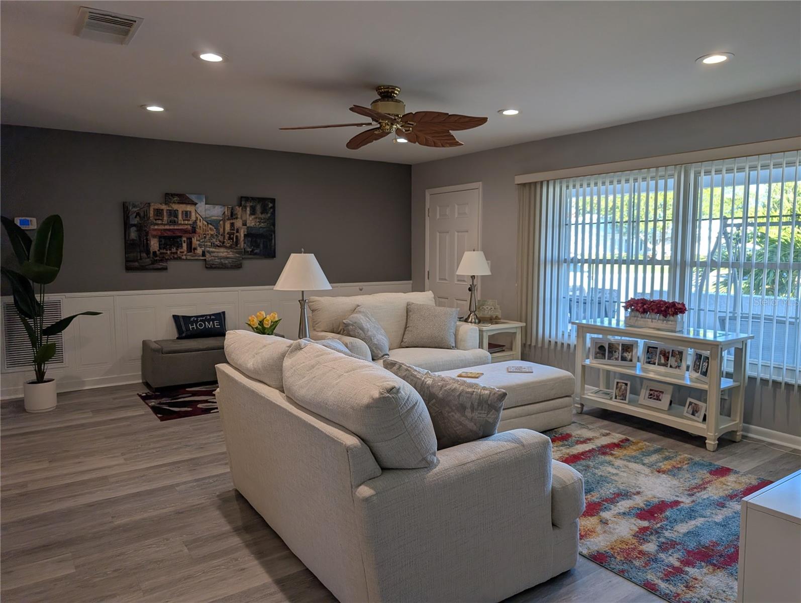 View of living room to front entry from hallway. Completely renovated in 2005 to studs, interior renovated again in 2023...neutral gray decor, wainscoting, beautiful luxury vinyl flooring, removal of popcorn ceilings, new ceiling fans, recessed lighting.