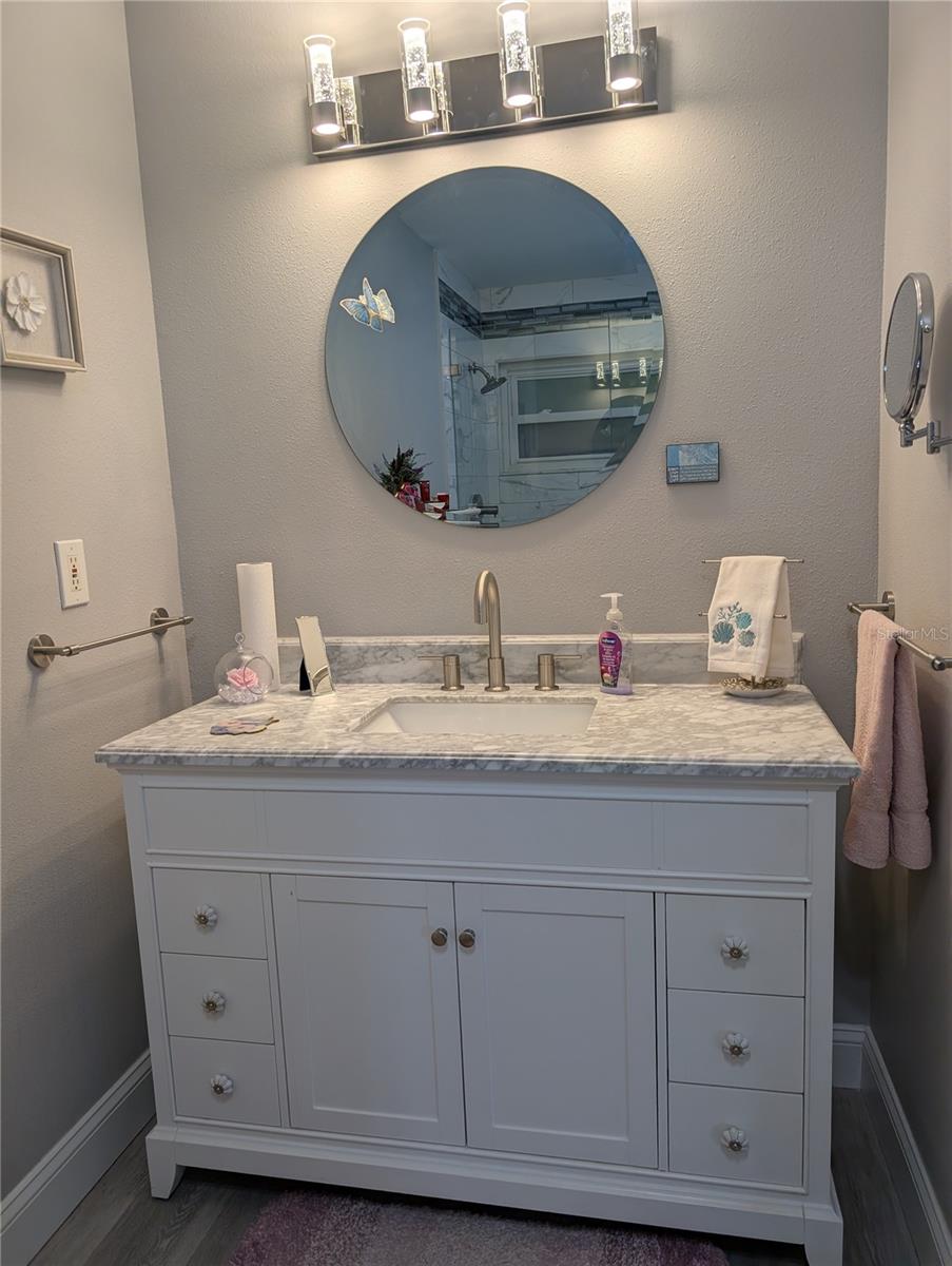 Totally renovated primary bath (2023) features vanity with marble sinktop, luxury vinyl, new mirror, light fixture and satin nickel hardware.flooring, mirror, light fixture, hardware and faucets.