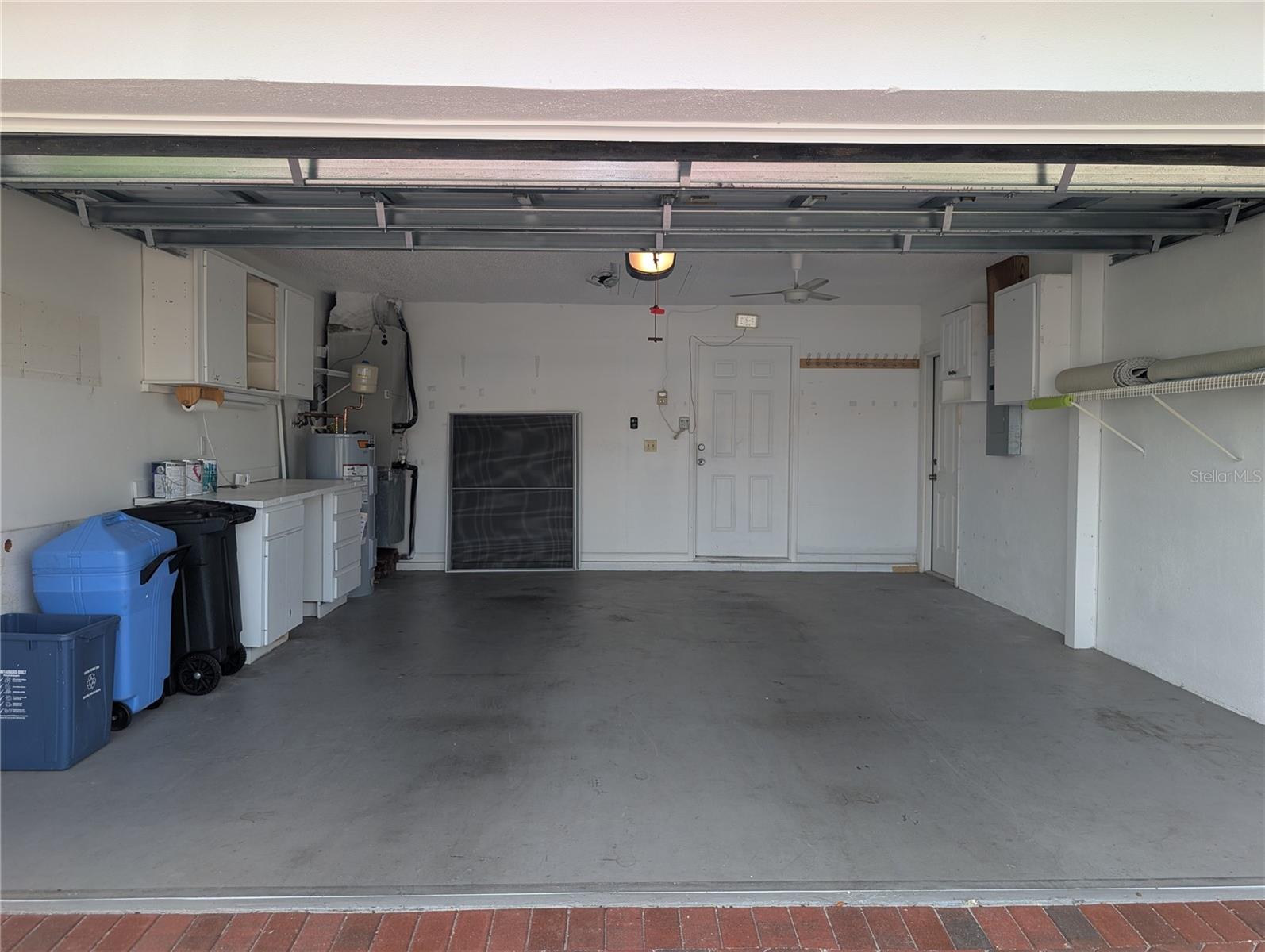 View of garage from other side of kitchen door. Garage offers a work bench, pull down ladder access to attic, Nordyne Frigidaire 3 ton HVAC w/heat pump installed 2010 (compressor updated 2016), State 40-gallon hot water heater (2025), workbench and access door to side yard.