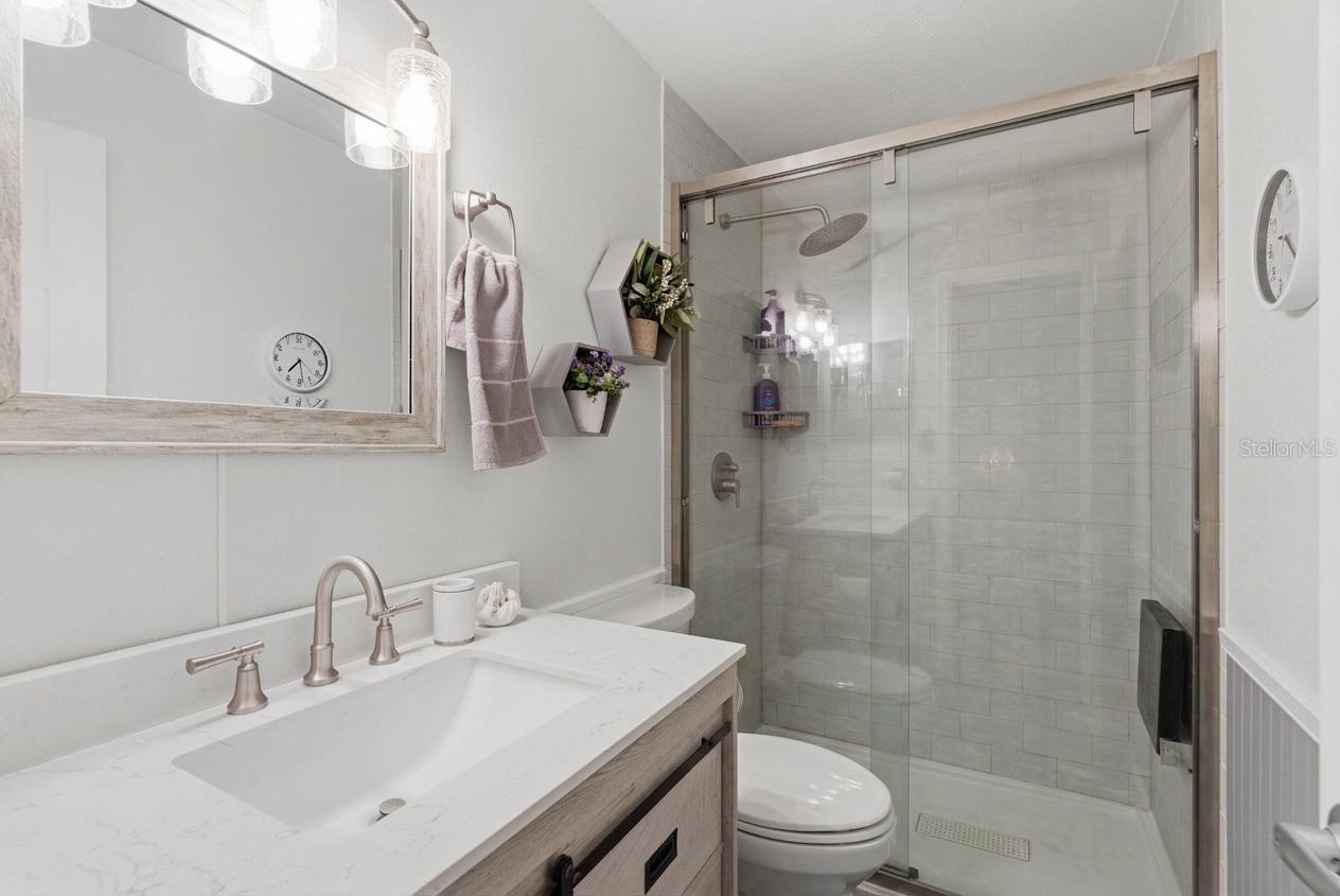 Beautifully updated primary ensuite with a walk-in shower, glass doors, modern finishes, and a farmhouse-inspired vanity detail.