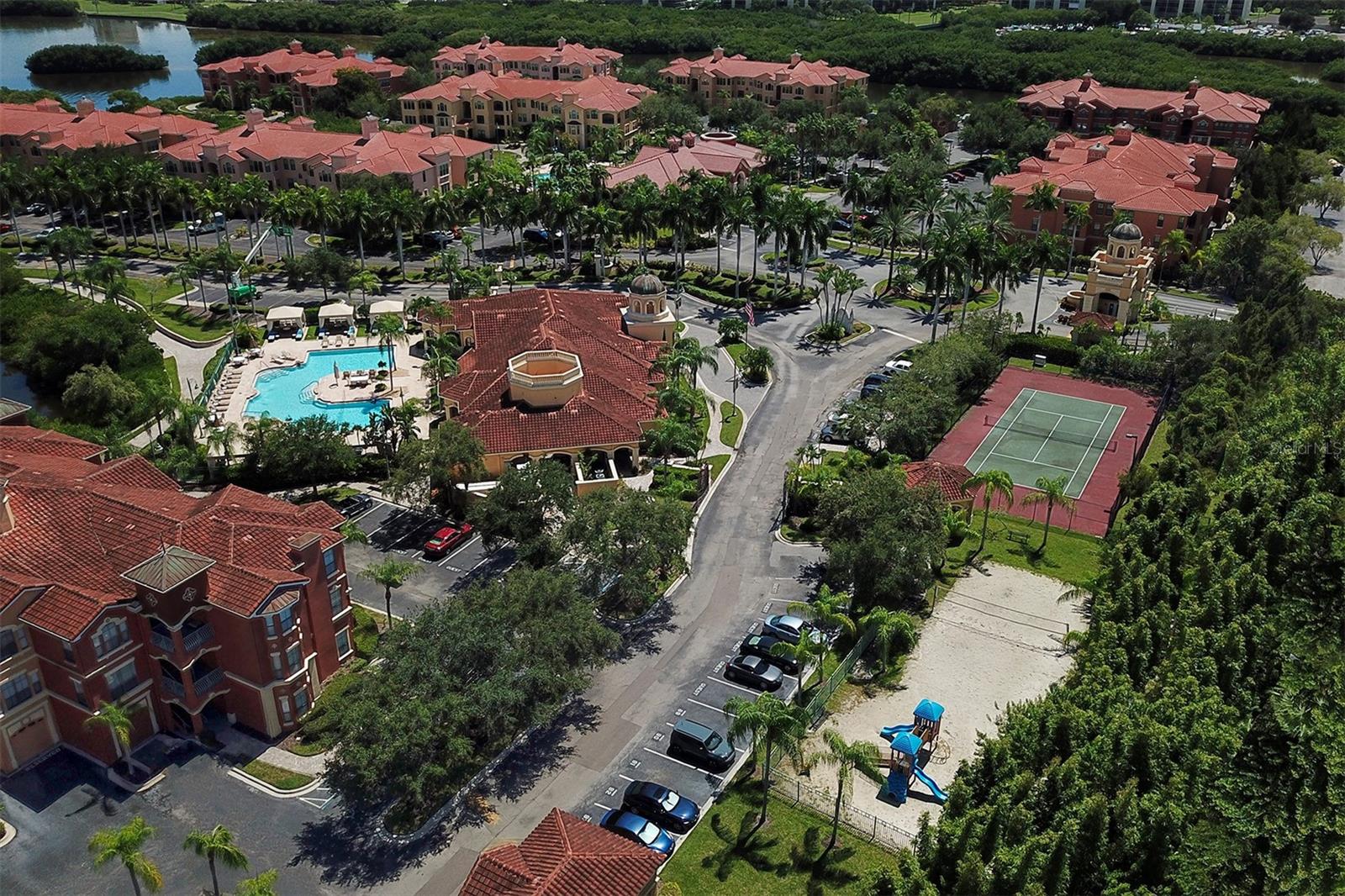 Aerial photo of the clubhouse and pool to the left, playground and sand volleyball court to the right and tennis court and guardhouse toward the top right