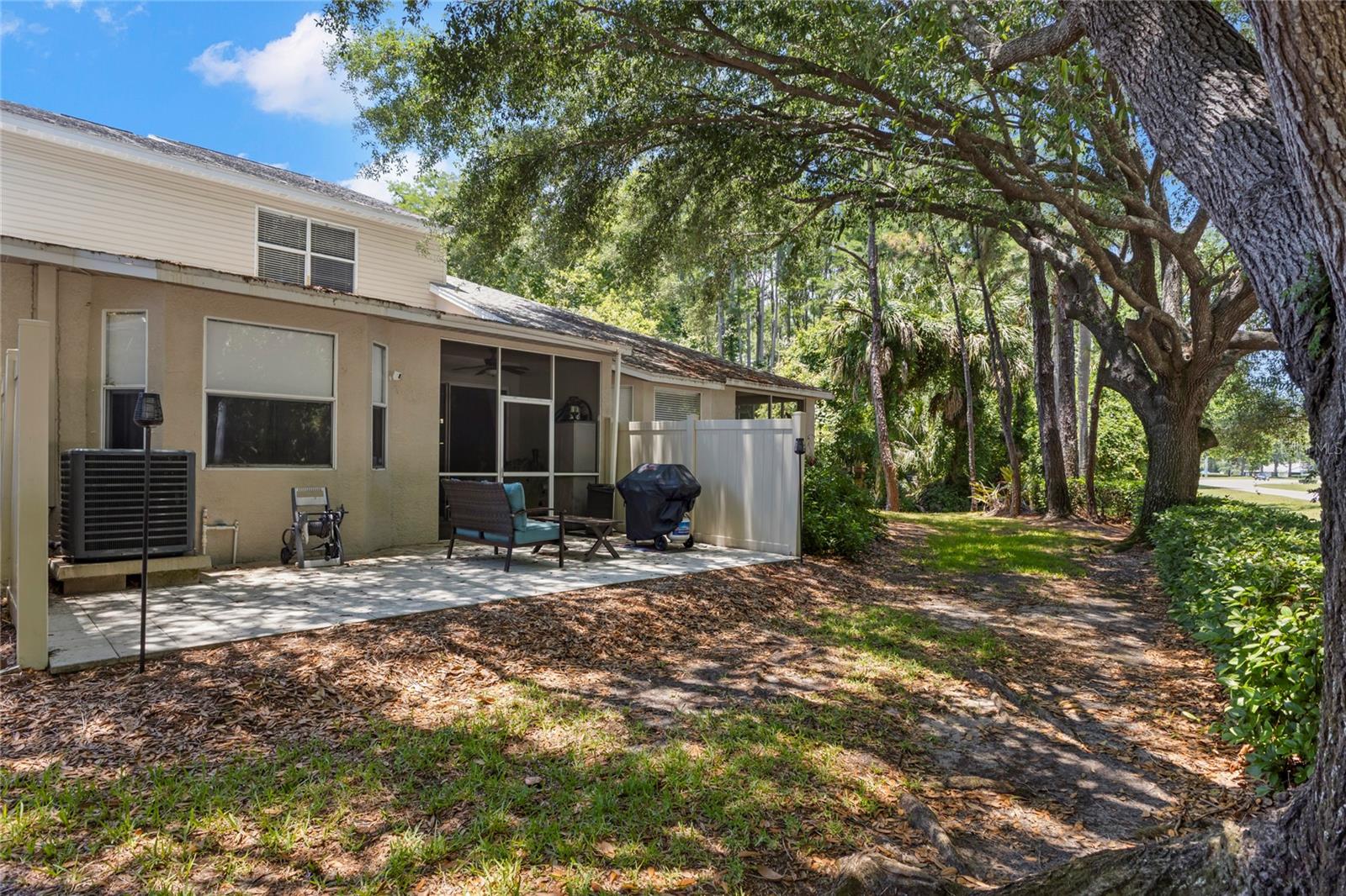 Rear exterior featuring a screened porch, extended paver patio, privacy fencing, and mature oak trees creating a shaded natural setting. The outdoor space offers flexibility for grilling, seating, and enjoying the surrounding greenery.
