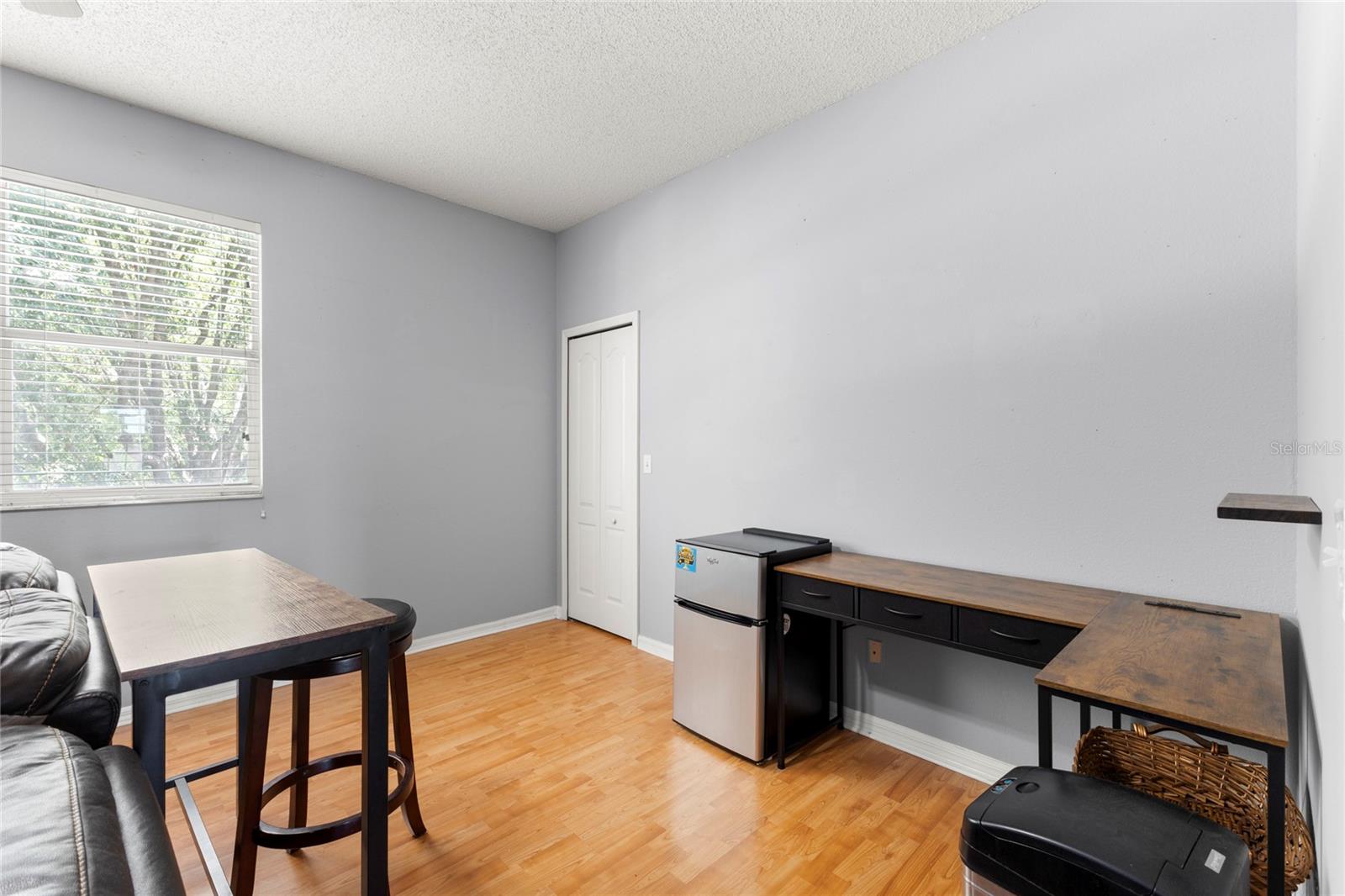 Second-floor loft/media room with warm wood-look flooring, neutral paint tones, oversized window with natural light, and walk-in closet access for additional storage. The flexible layout easily accommodates a media setup, workspace, gaming area, or lounge seating.