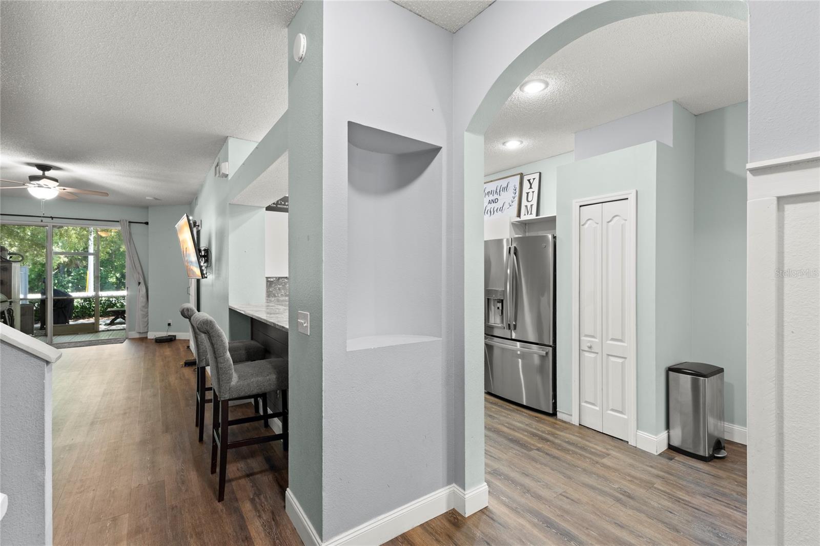 Open-concept layout with arched entryways, recessed niches, neutral interior paint, and wood-look laminate flooring flowing throughout the main living spaces. Sightlines extend from the foyer through the living area to the screened rear porch, enhancing the home’s open feel and natural light.