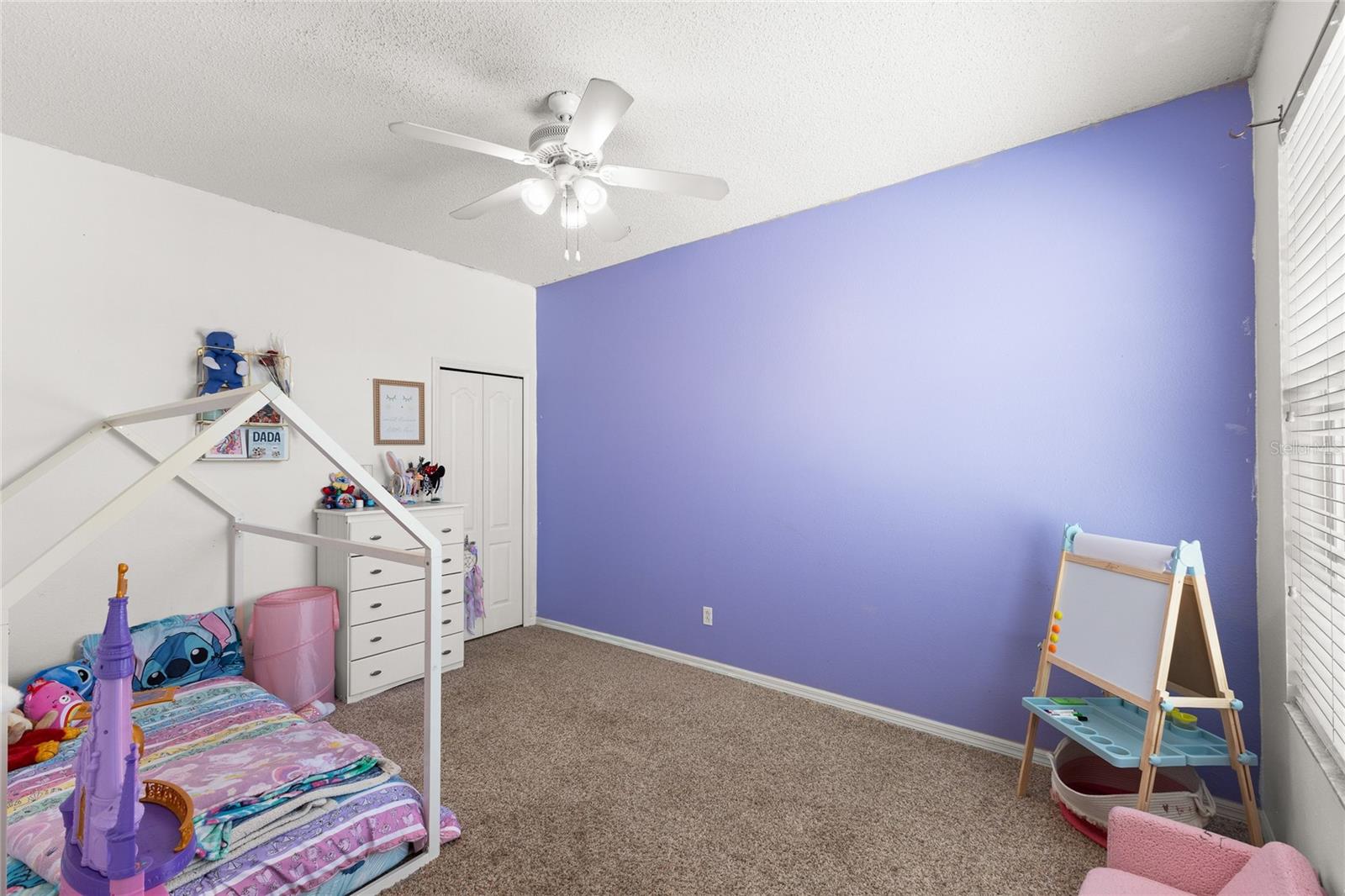 2nd bedroom with carpeted flooring, walk-in closet, ceiling fan with light kit, and oversized window providing natural light. Spacious layout offers flexibility for bedroom furnishings, guest accommodations, nursery, or playroom use.