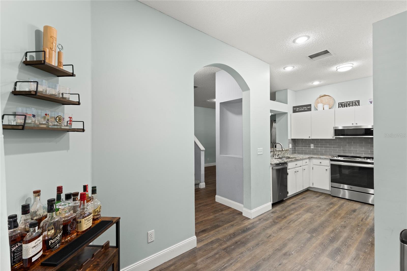 Kitchen with white cabinetry, granite countertops, stainless steel appliances, recessed lighting, and a gray subway tile backsplash. The open floorplan and arched transitions create an airy, connected feel throughout the main level.