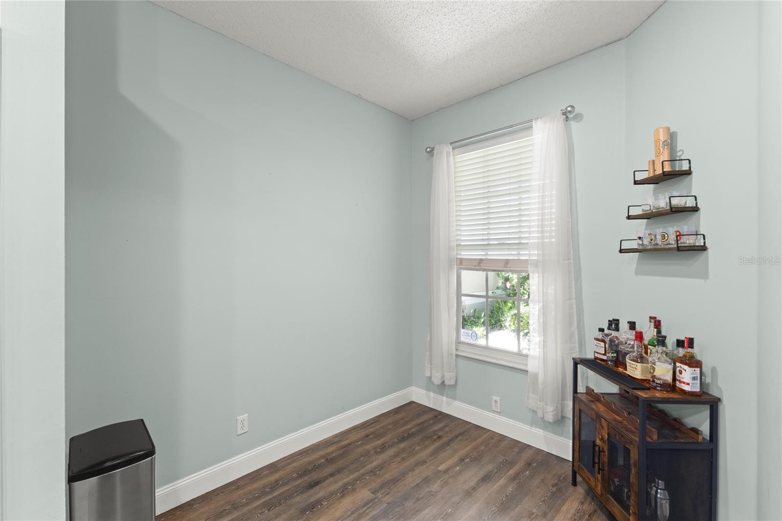 Casual kitchen dining space with wood-look laminate flooring, soft neutral tones, and a large window providing natural light. The flexible layout offers space for a breakfast table, coffee station, or additional seating.