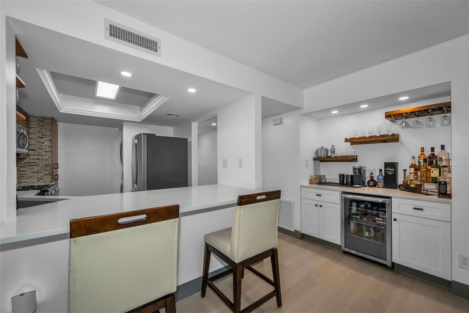 Another view of dry bar with wine refrigerator and storage cabinets, plus stools at open kitchen bar.