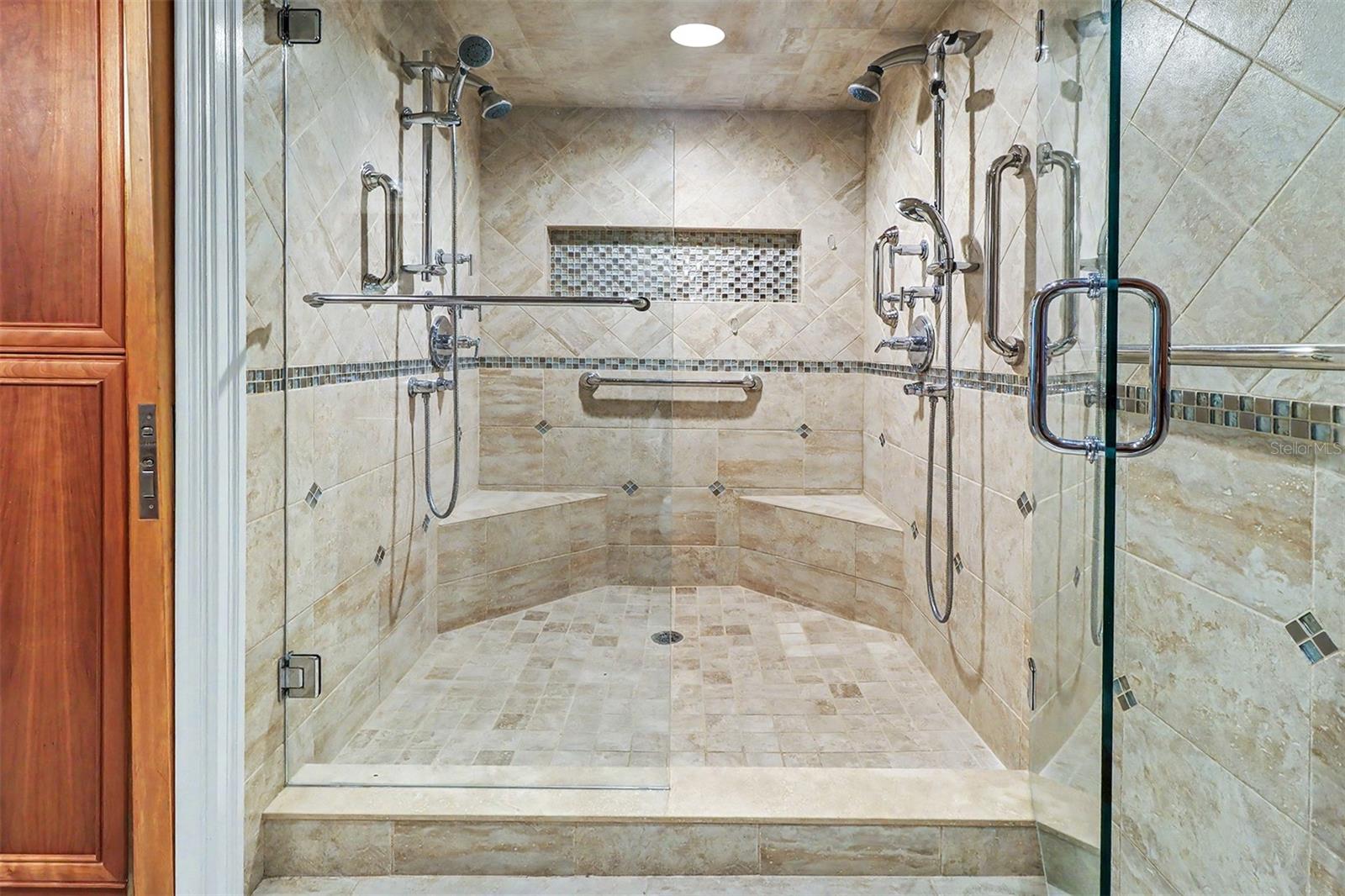 Indulge in the spa-inspired walk-in shower, beautifully finished with custom tile, built-in bench seating, dual shower heads, handheld sprayers, body jets, and discreetly integrated safety grab bars.