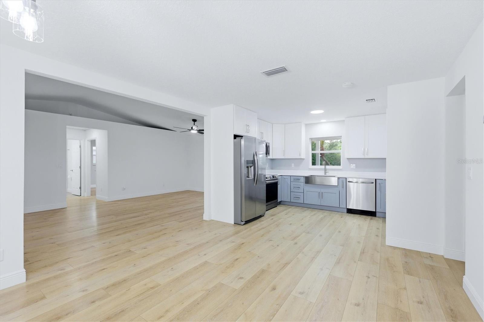 View from dining are into kitchen and living area.  Kitchen features modern cabinetry in two tones plus a farm style sink