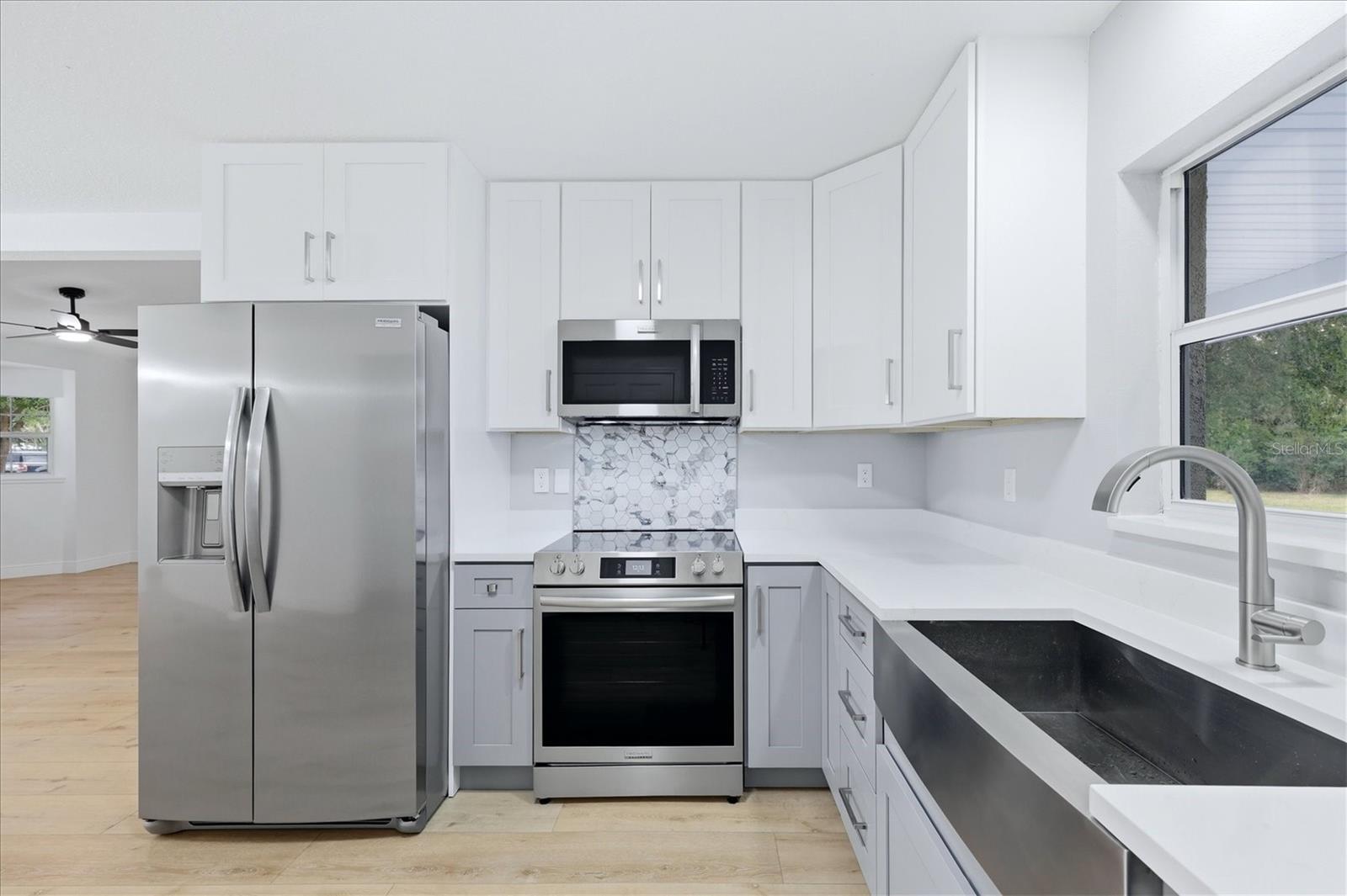 Quartz countertops with a slight marbling and a geometric tile backsplash over the range coordinate nicely with the cabinetry.