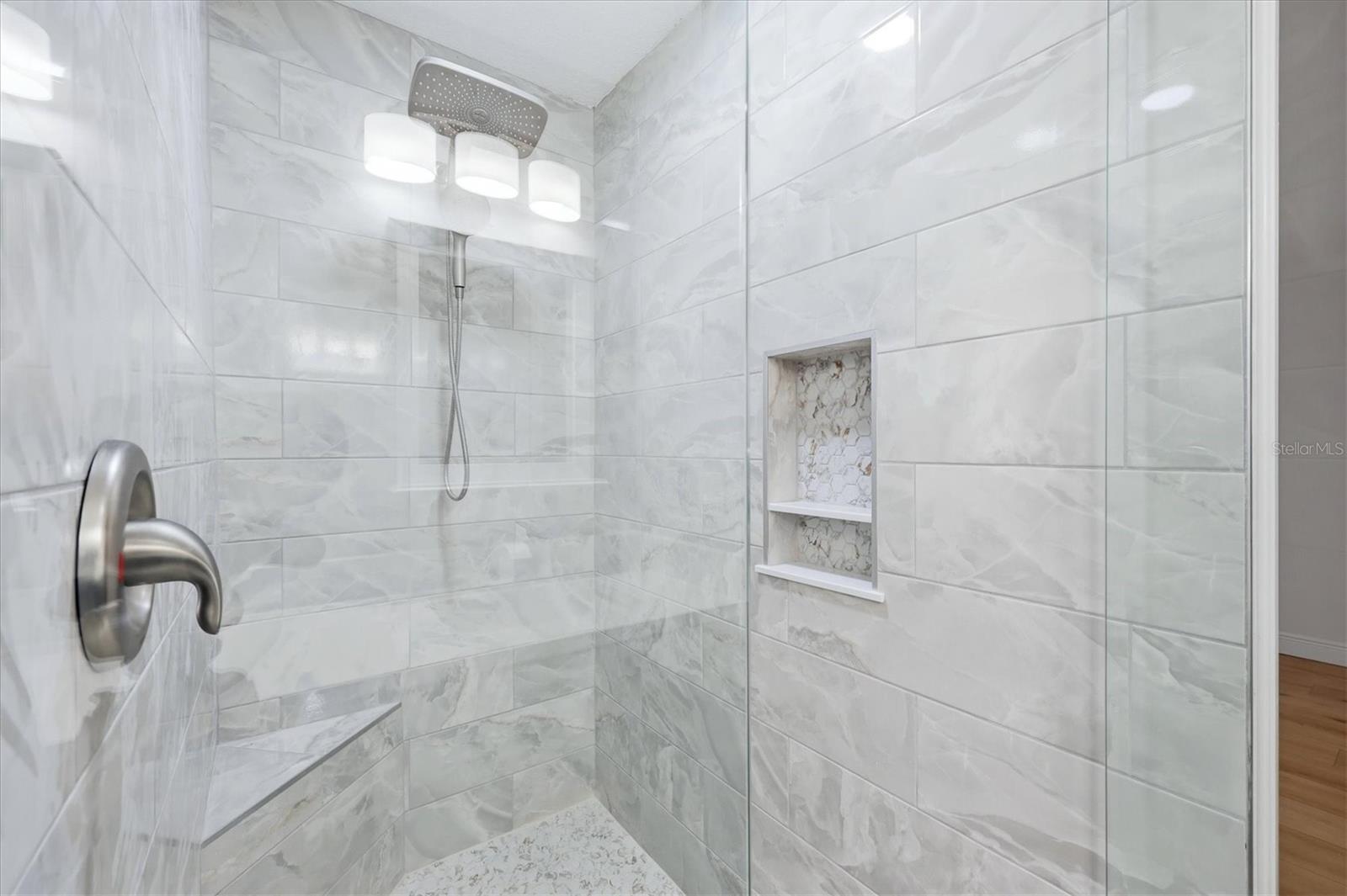 Decorator tiles adorn the walk-in shower featuring a corner seat, product shelf & Delta faucet and dual shower head,